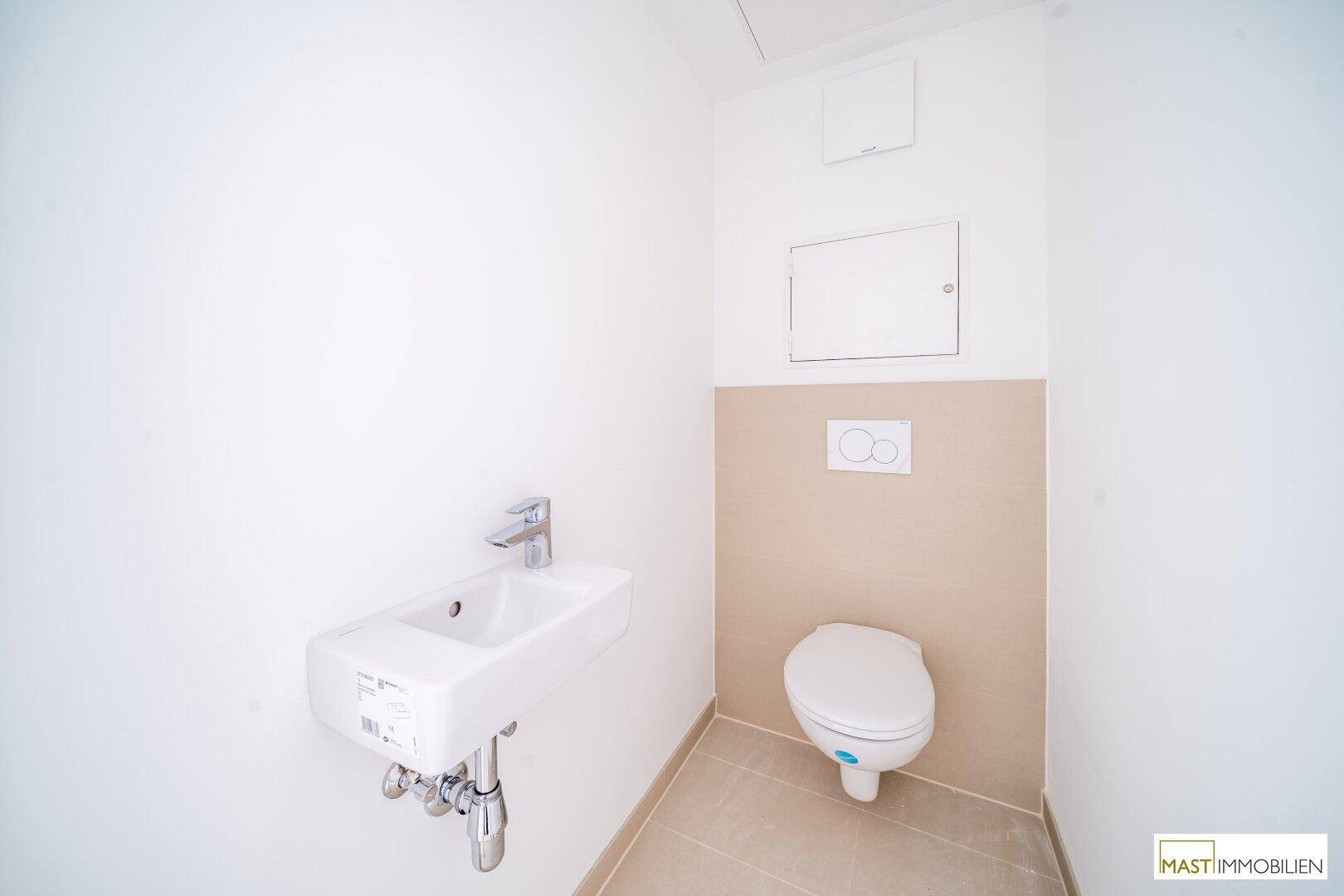 Kleines Gäste-WC mit Wand-WC, kleinem Waschbecken und beigefarbenen Wandfliesen.