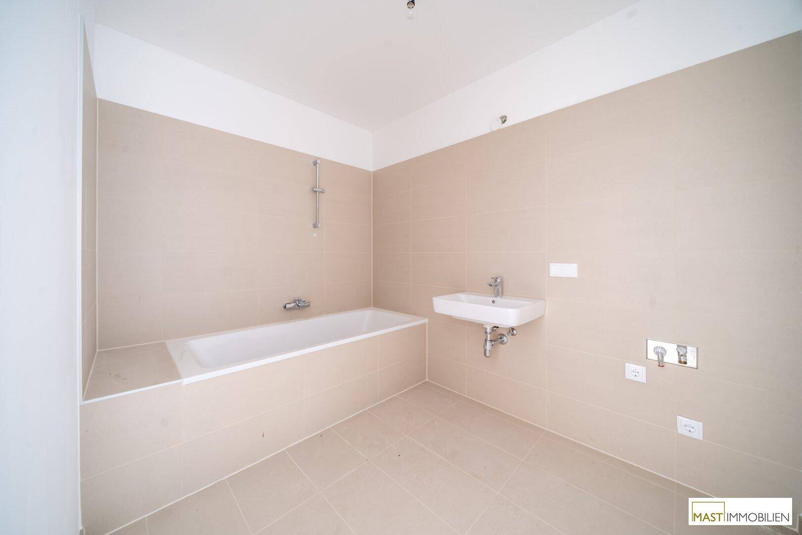 Modernes Badezimmer mit beigefarbenen Fliesen, einer Badewanne und einem einzelnen Waschbecken.
