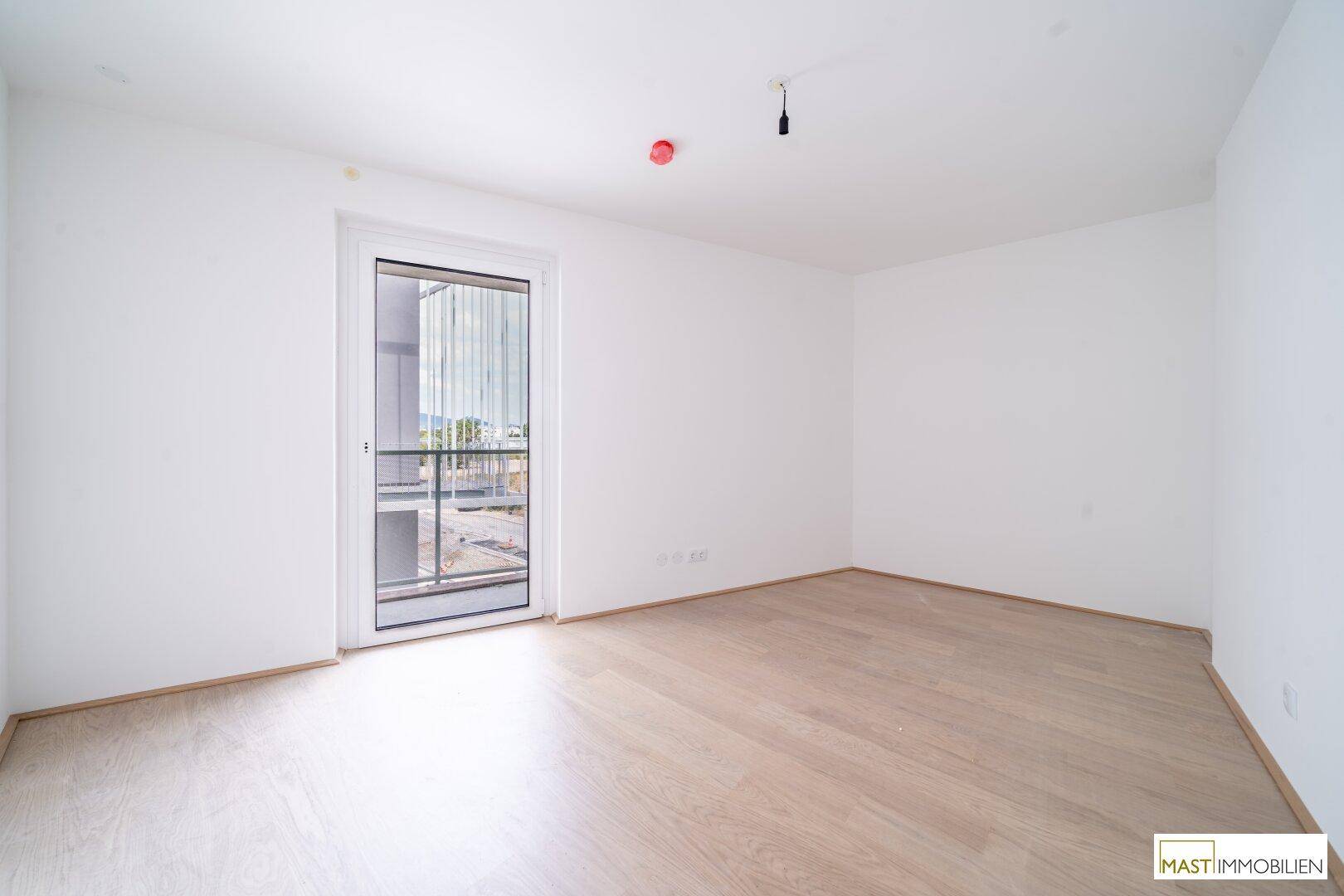 Helles Schlafzimmer mit Holzboden und Zugang zu einem kleinen Balkon oder einer französischen Tür.