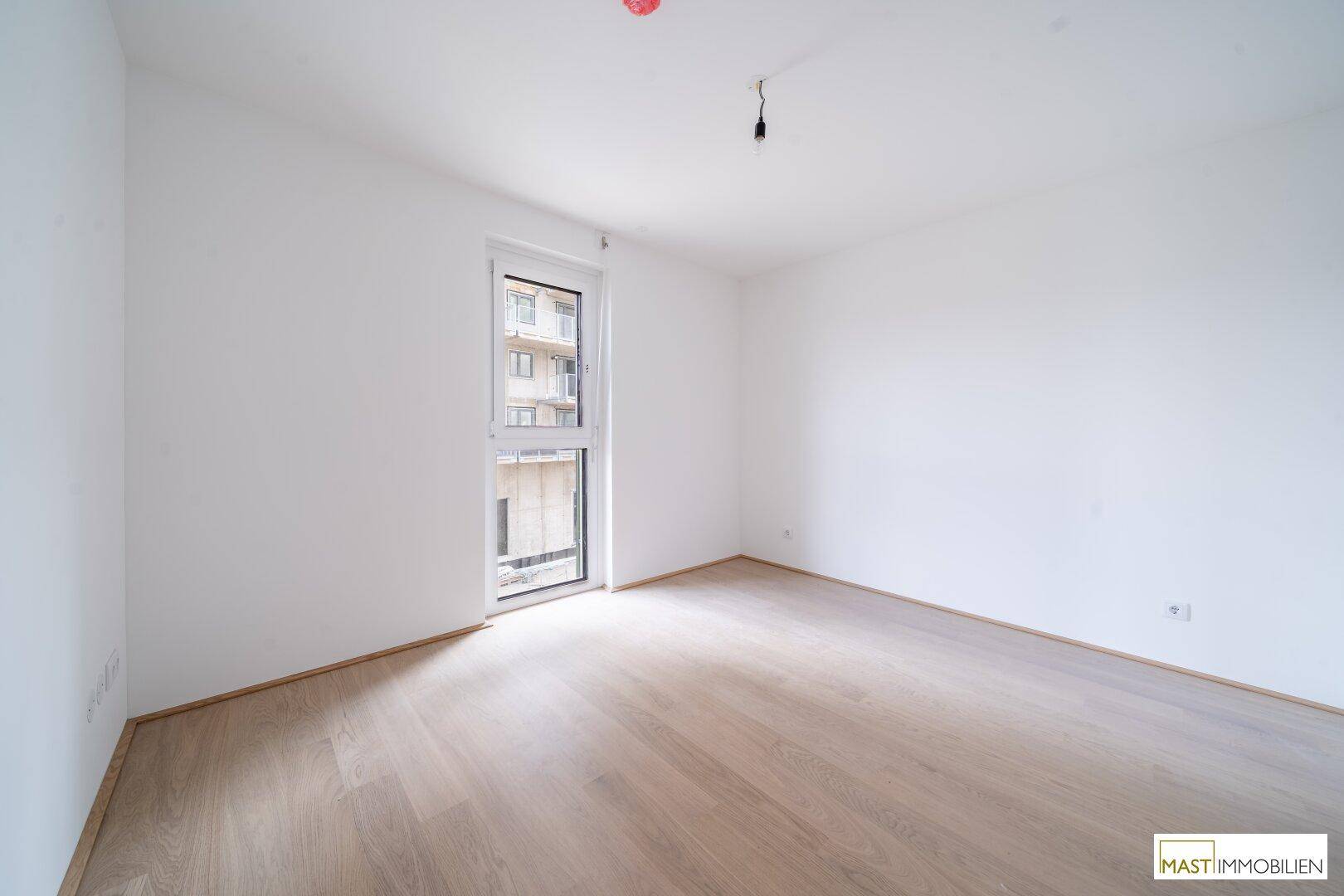 Weiteres Schlafzimmer mit hellem Holzboden und einem Fenster, das den Blick nach draußen freigibt.