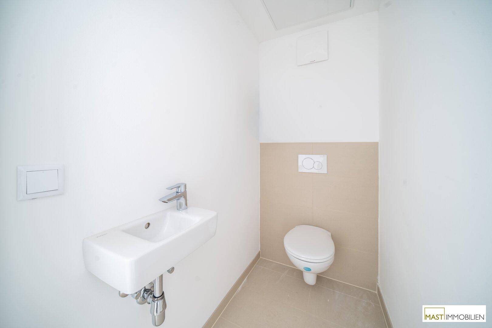 Separates Gäste-WC mit wandhängender Toilette und kleinem Waschbecken, halbhoch gefliest.