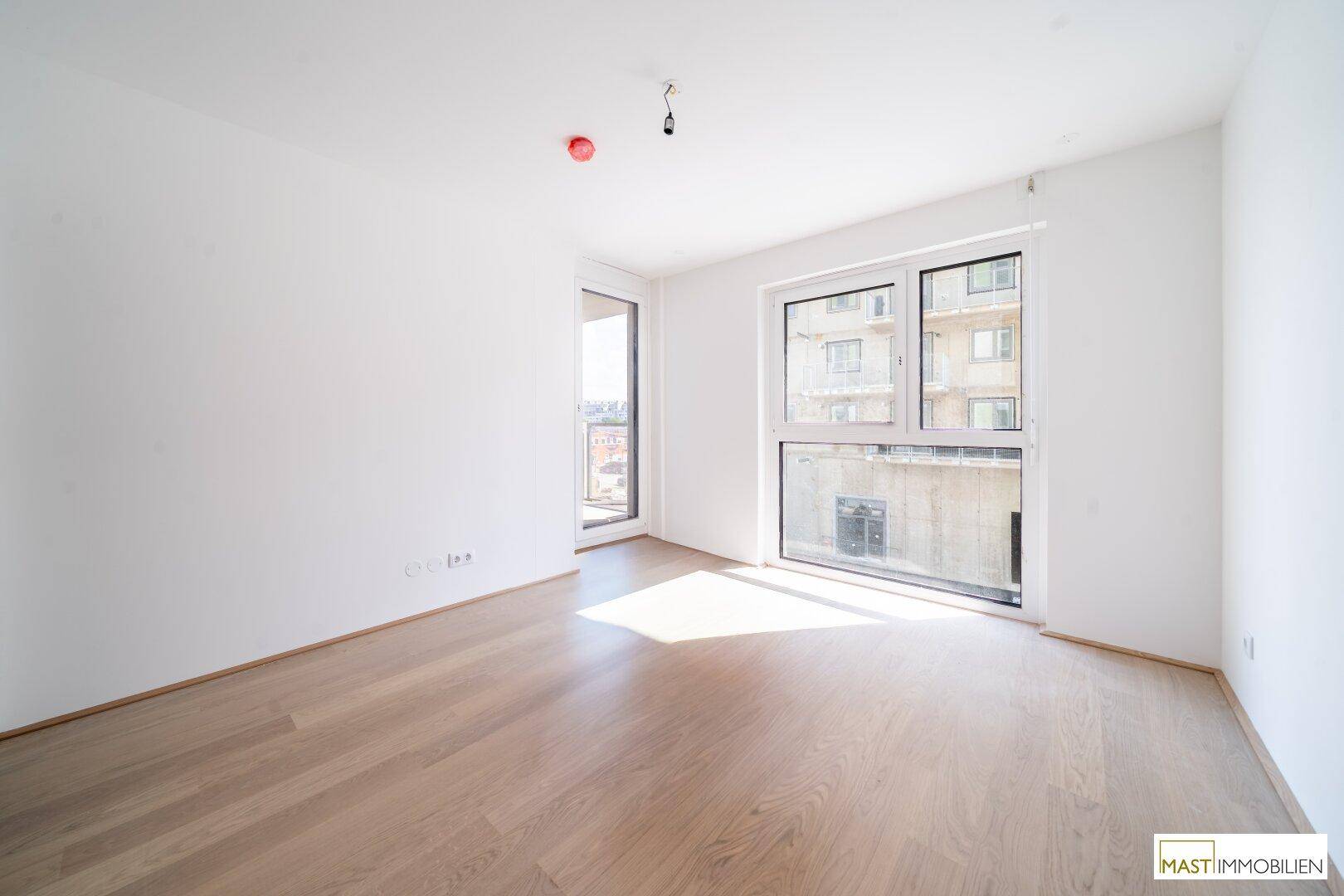 Helles Zimmer mit neuem Parkettboden und Zugang zu einem Balkon, mit Blick auf die umliegende Bebauung.