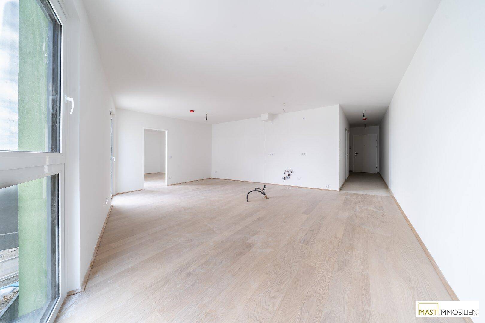 Großer, leerer Wohnraum mit hellen Holzböden und viel Tageslicht durch die Fenster.