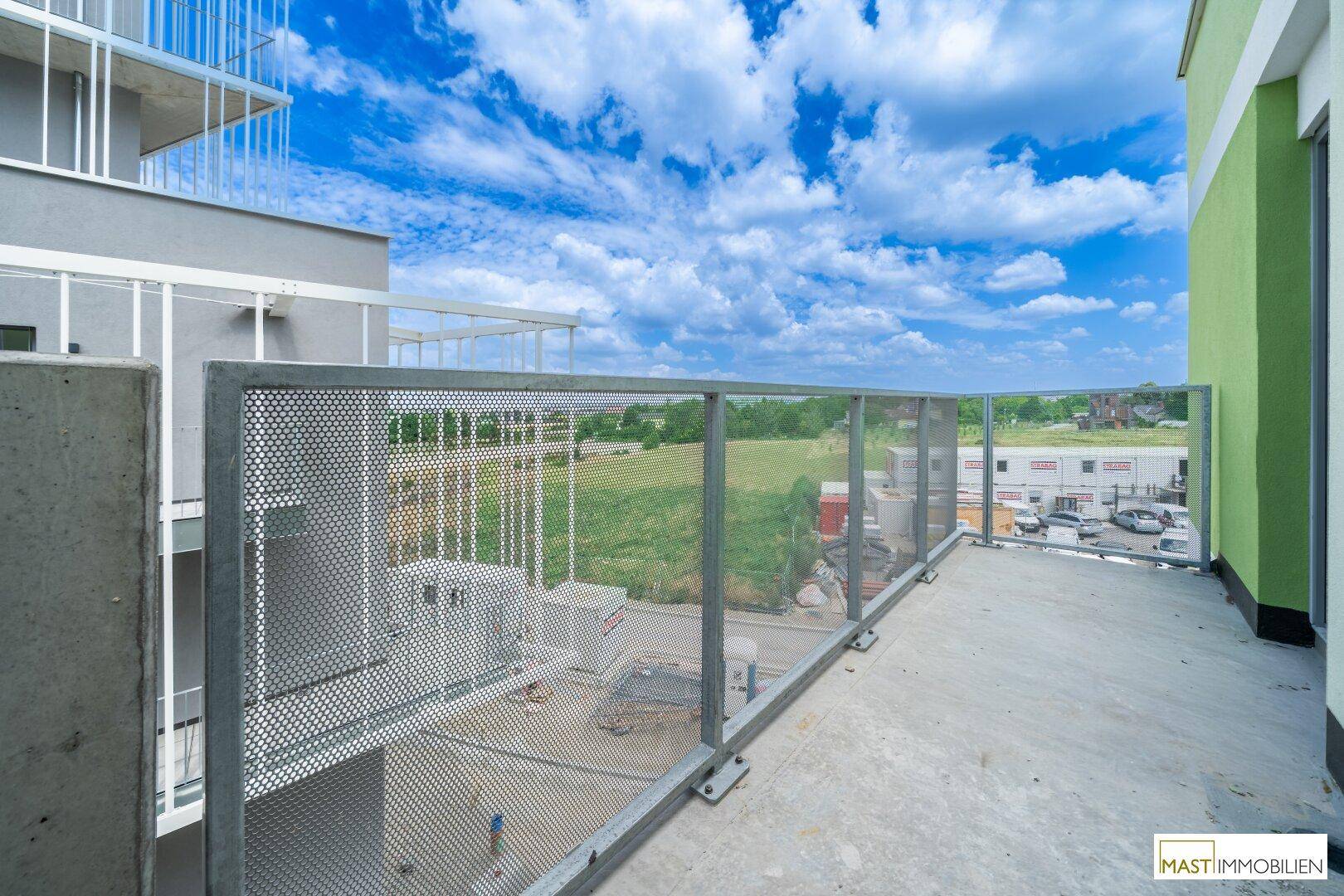 Geräumiger Balkon mit Metallgeländer und weitem Blick über grüne Felder.