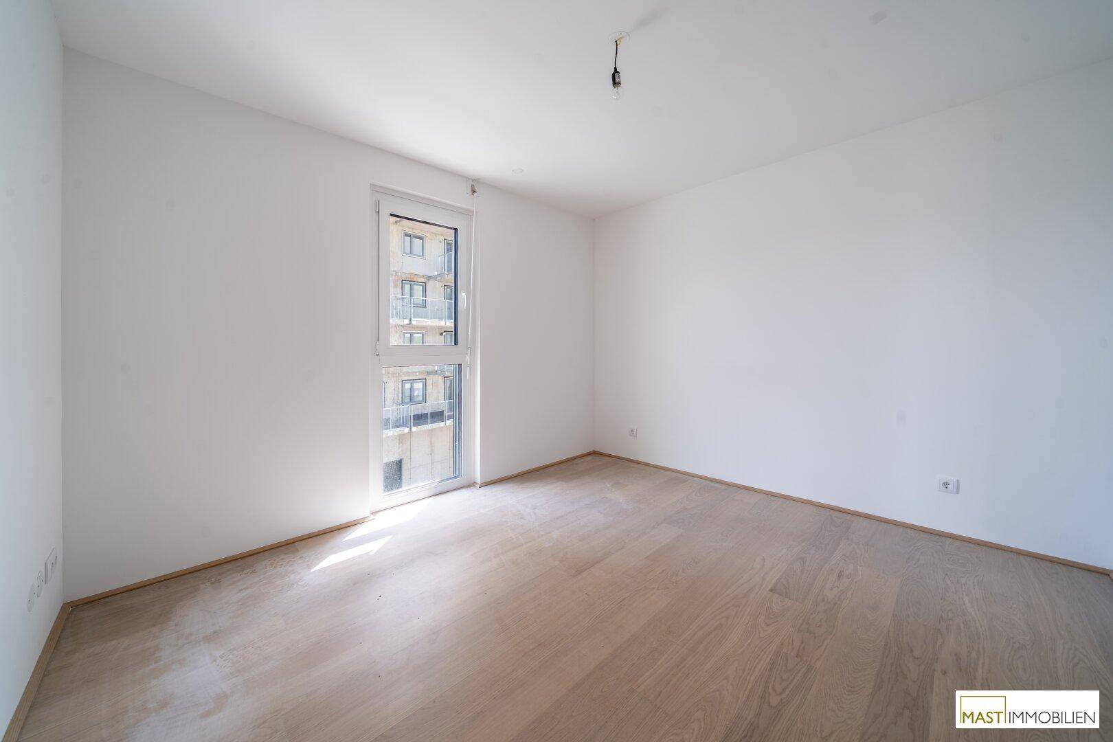 Unmöbliertes Schlafzimmer mit hellem Holzboden und einem Fenster mit Blick nach draußen.