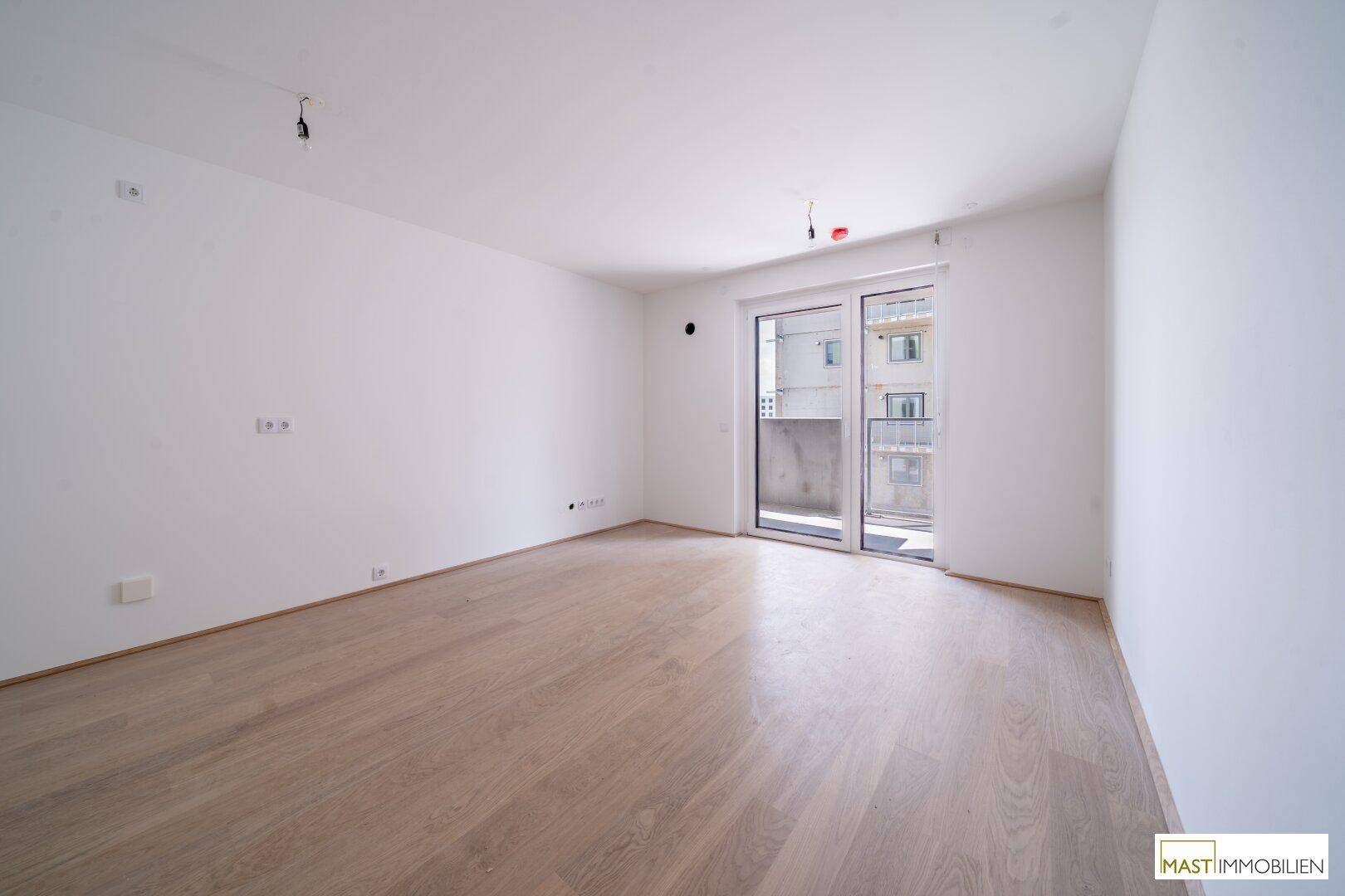 Helles Zimmer mit Holzboden und Zugang zu einem Balkon, ideal als Wohn- oder Schlafbereich.