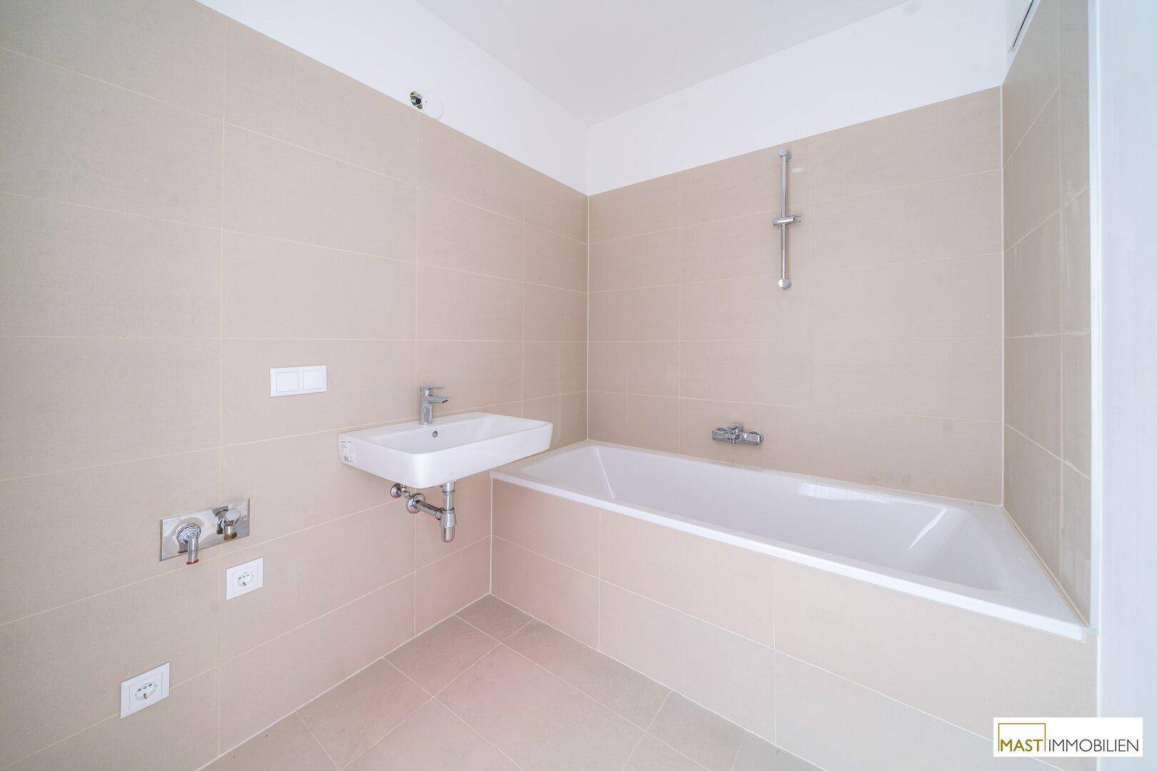 Modernes Badezimmer mit beigefarbenen Fliesen, einer Badewanne und einem Waschbecken.