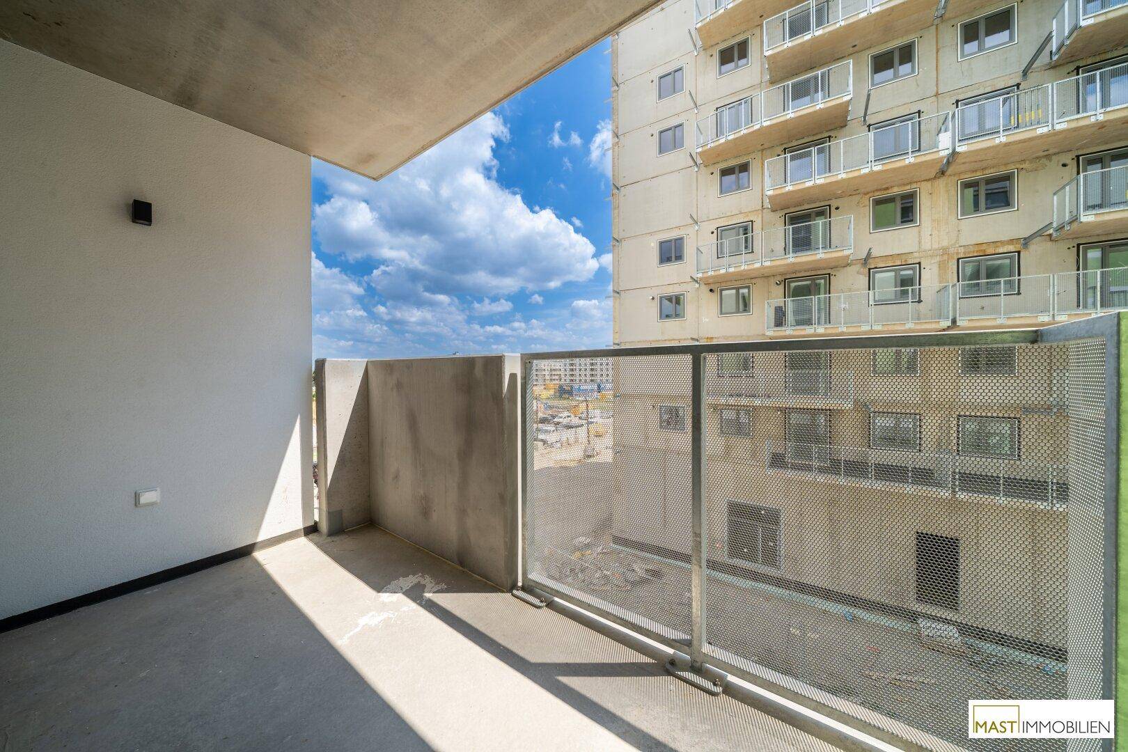Geräumiger Balkon mit Betonboden und Metallgeländer, bietet Blick auf umliegende Gebäude.