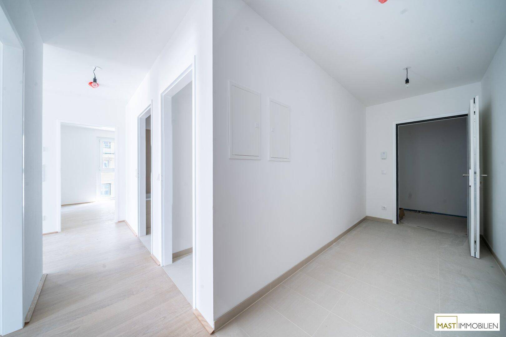 Helle Diele mit modernem Parkettboden und Zugang zu mehreren Zimmern in einem Neubau.