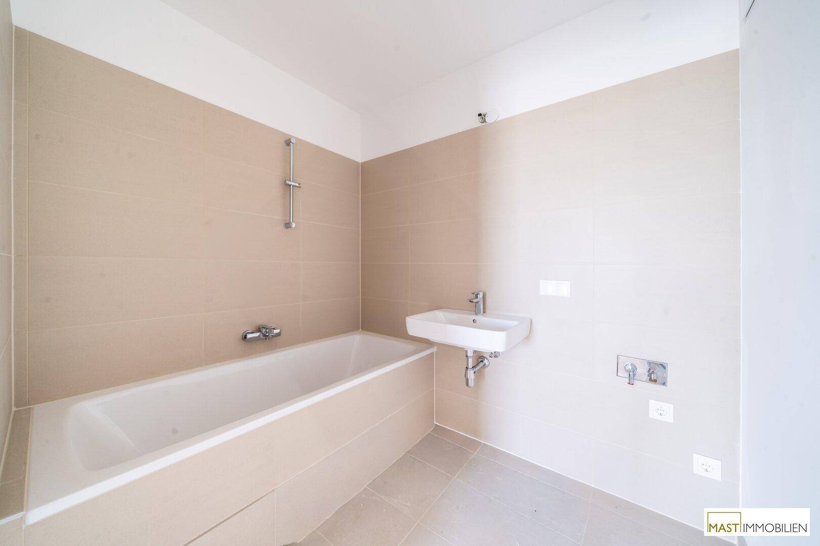 Modernes Badezimmer mit Badewanne, Waschbecken und beigefarbenen Wandfliesen.