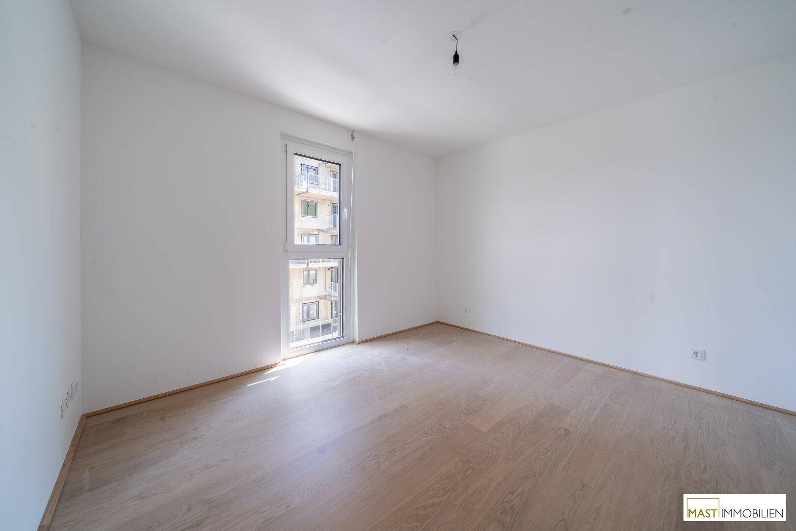 Weiteres helles Schlafzimmer mit Parkettboden und Blick auf die Umgebung.