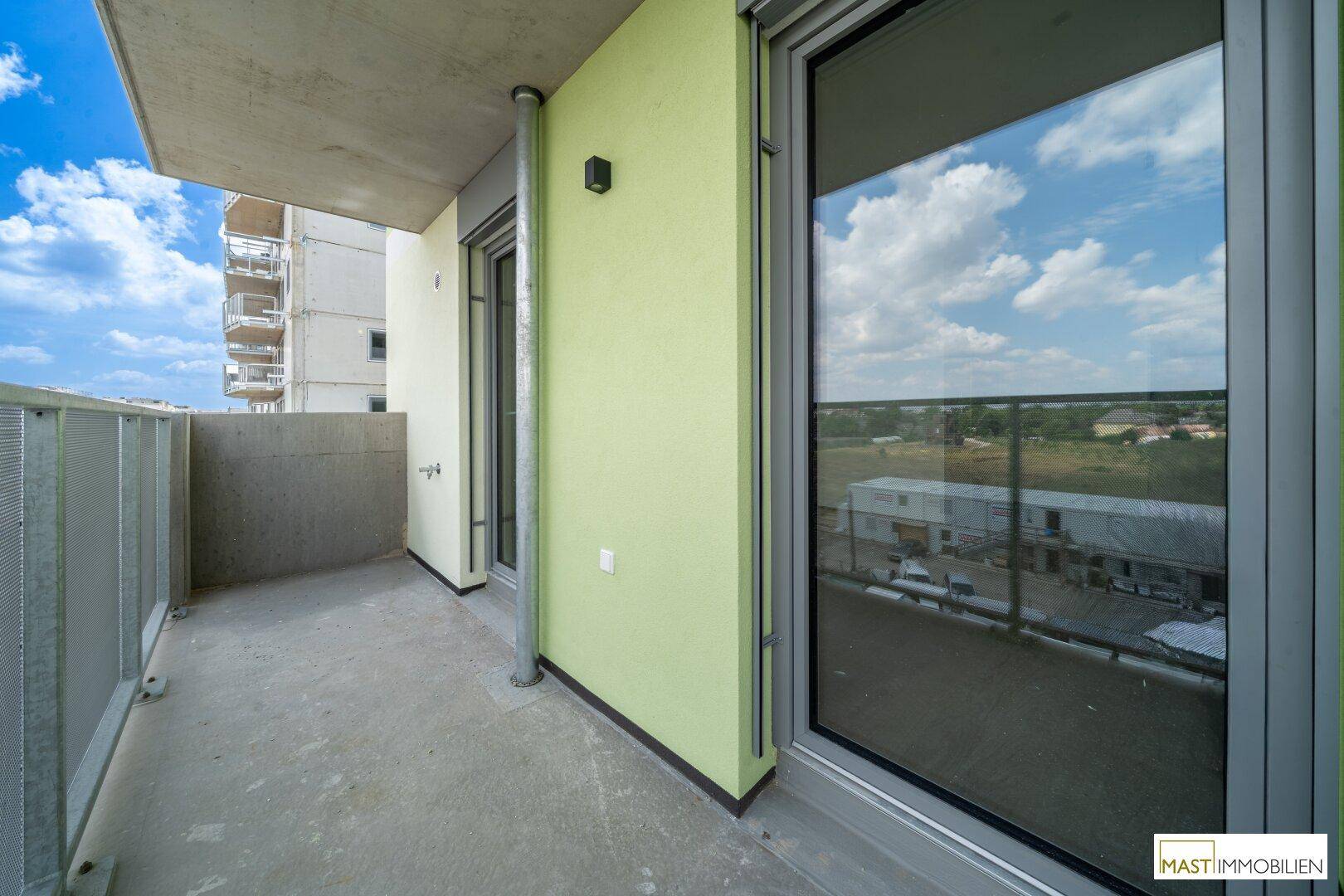 Balkon mit hellgrüner Fassade und großen Fenstern, die den Himmel reflektieren.