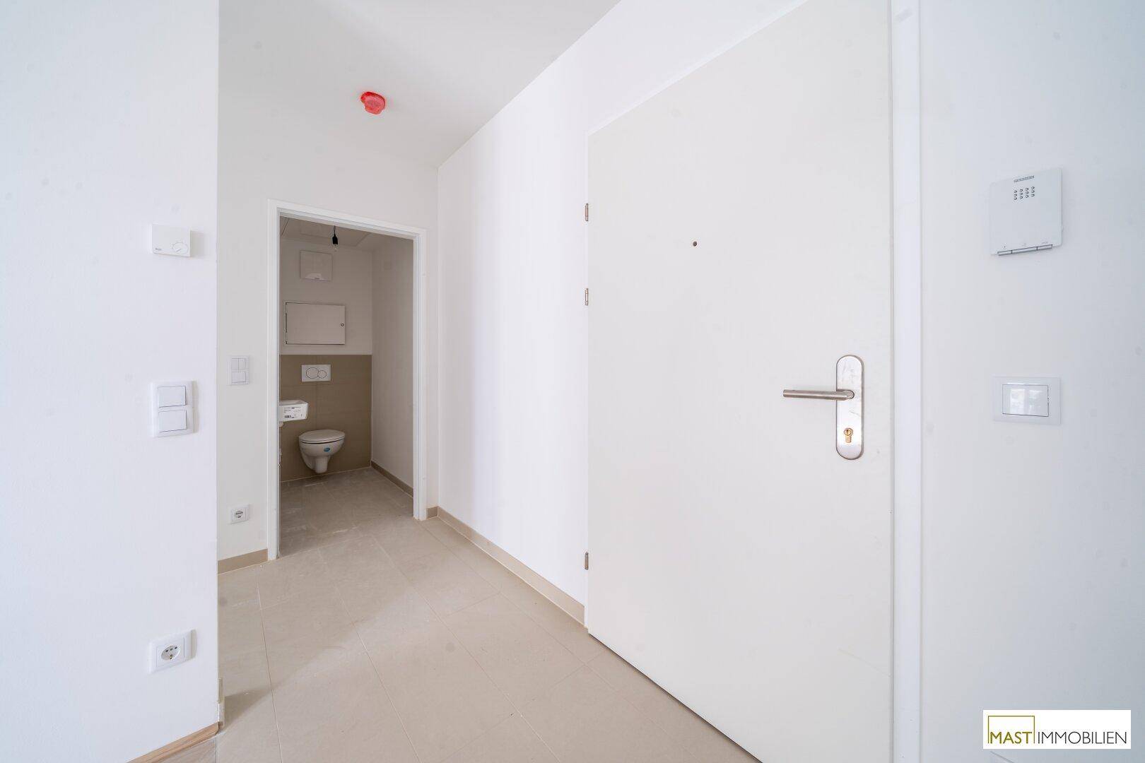 Heller Flur mit weißer Tür und Zugang zu einem Gäste-WC, ausgestattet mit Fliesenboden.