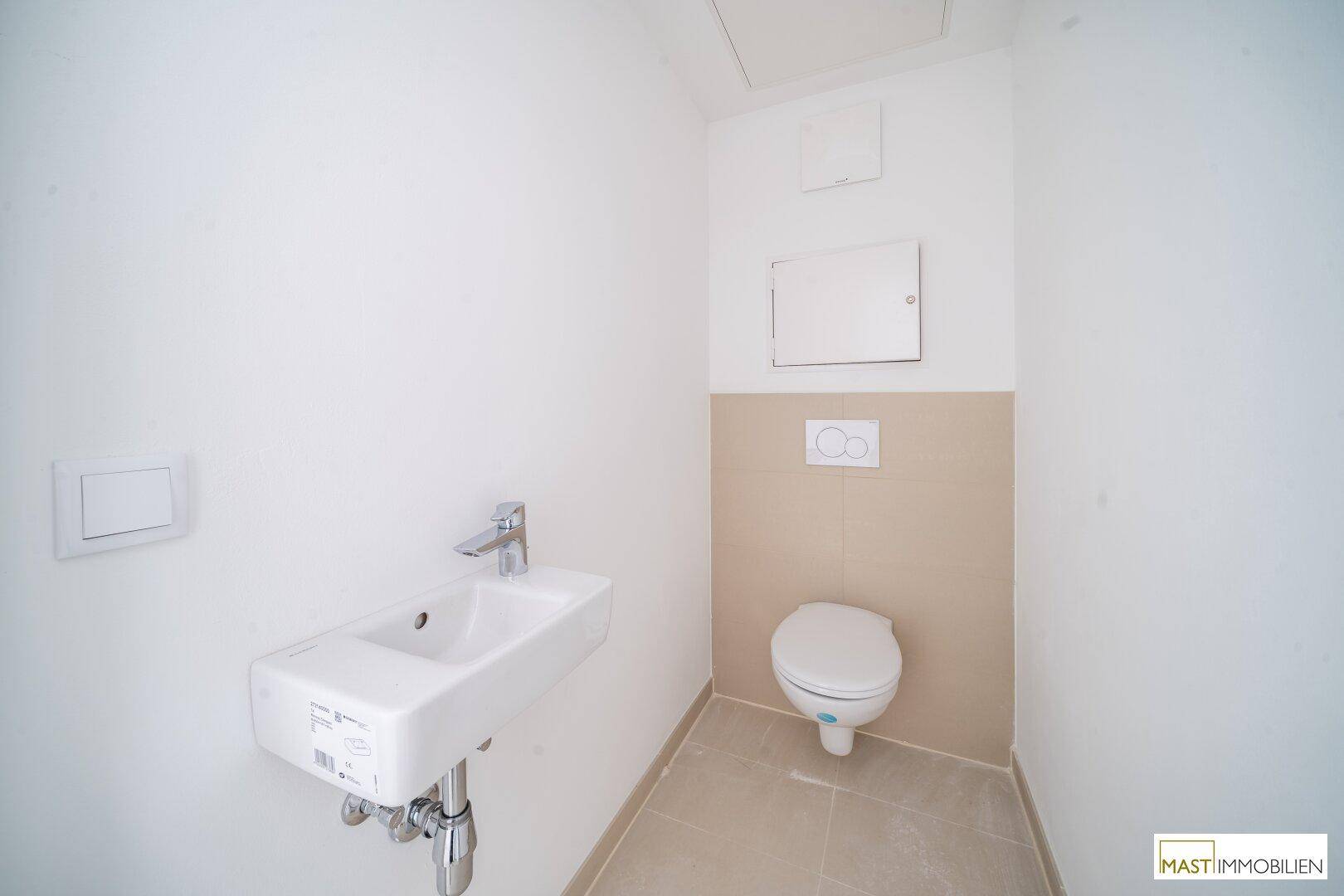 Funktionales Gäste-WC mit wandhängender Toilette, kleinem Waschbecken und hellen Fliesen.