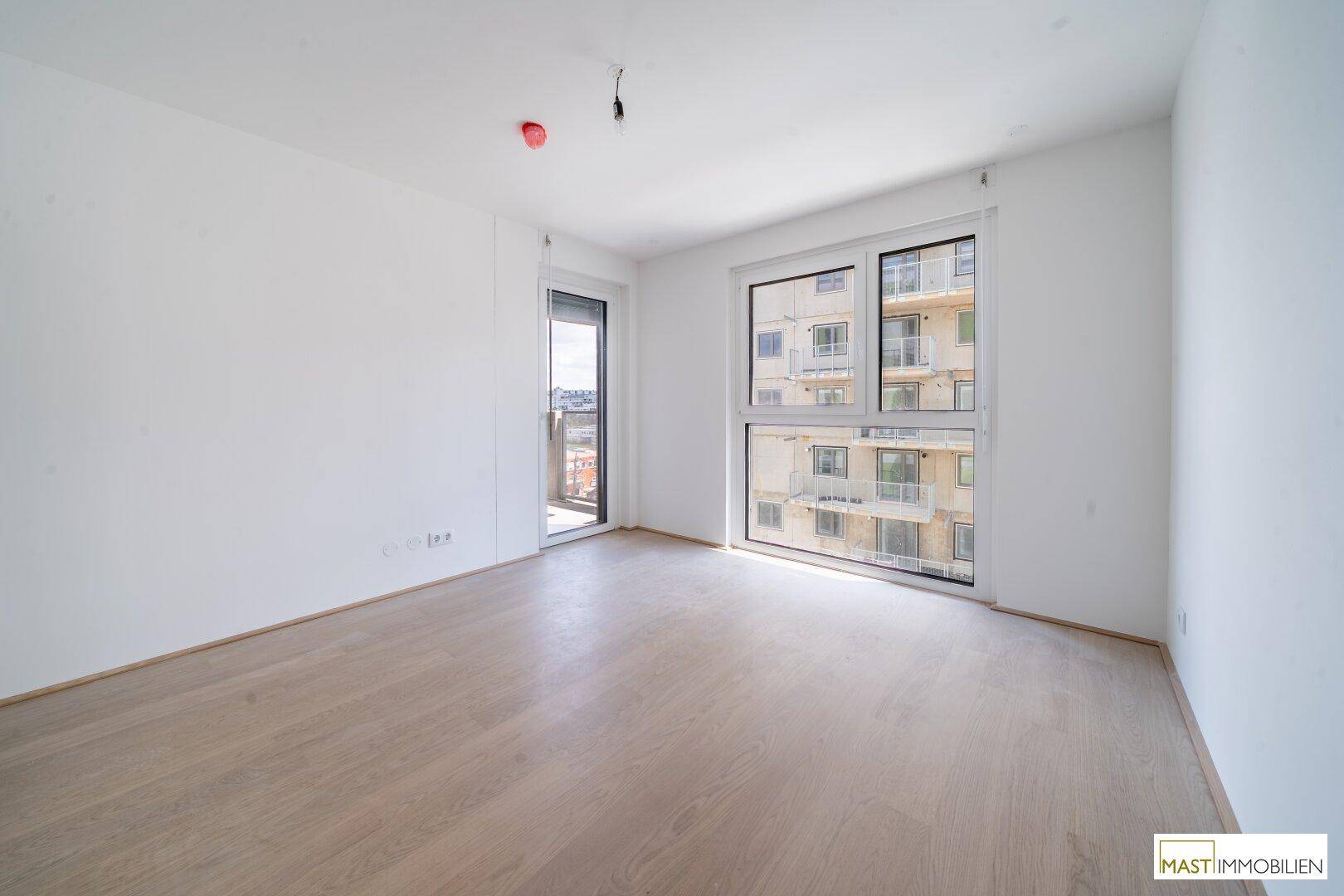 Lichtdurchflutetes Schlafzimmer mit großen Fenstern, Parkettboden und Zugang zum Außenbereich.