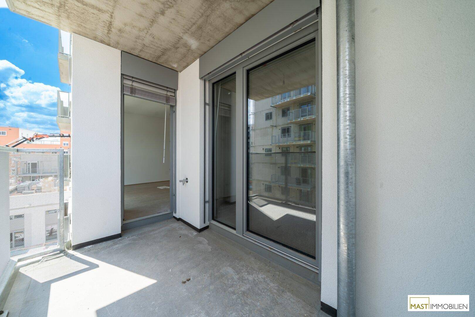 Heller Balkon mit Betonboden und großer Glasschiebetür, die zum Innenraum führt.