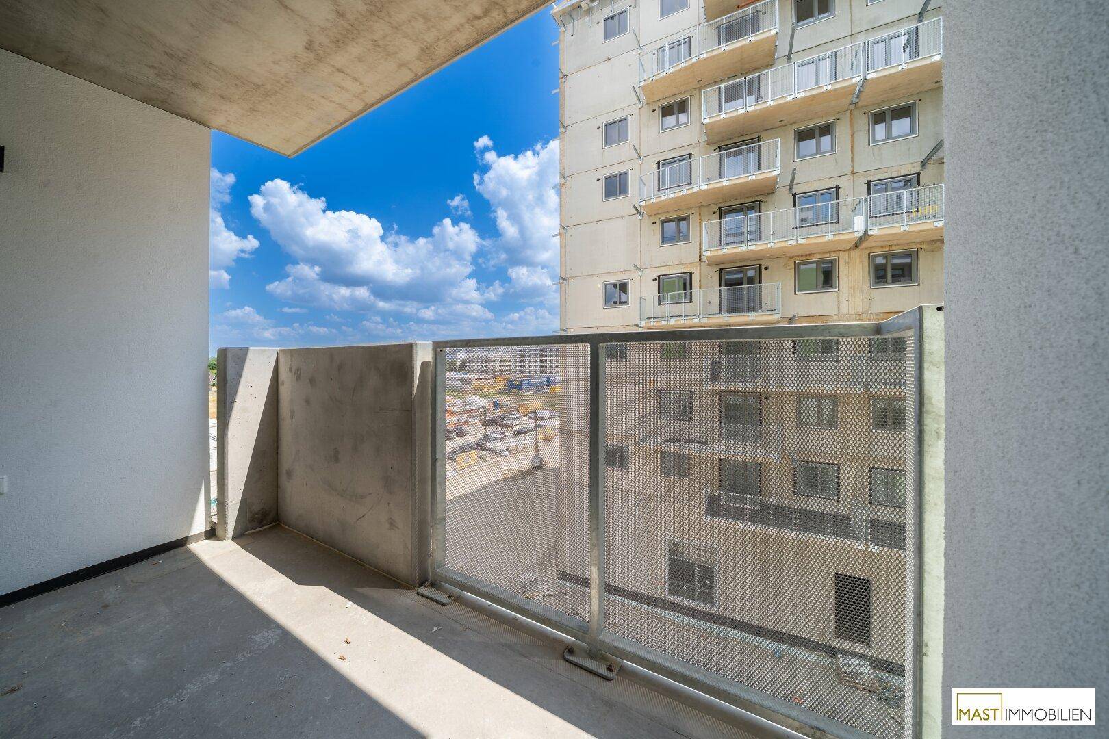 Geräumiger Balkon mit Betonboden und Metallgeländer, Blick auf angrenzende Neubauten.