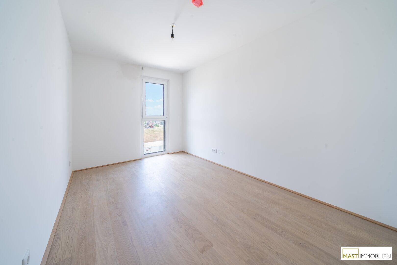 Gemütliches Schlafzimmer mit hellem Holzfußboden und einem großen Fenster, das viel Licht spendet.