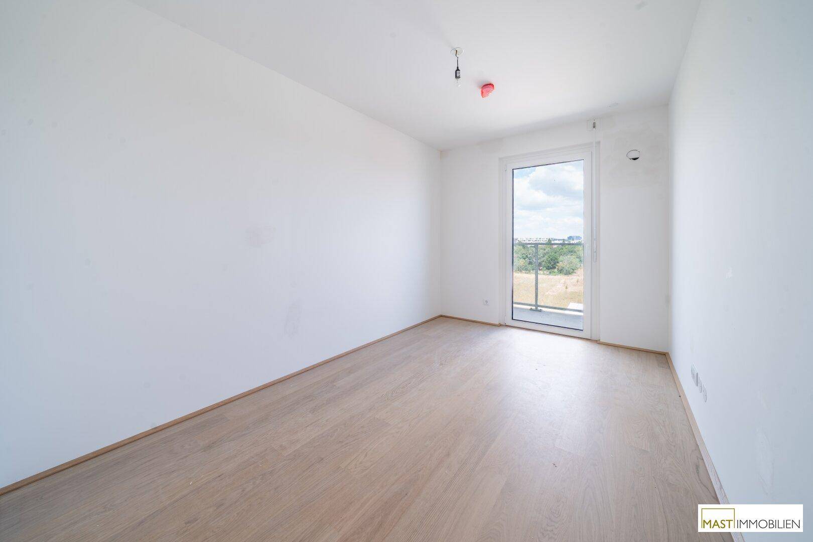 Helles Schlafzimmer mit Balkonzugang und hellem Holzfußboden, bietet einen angenehmen Ausblick.
