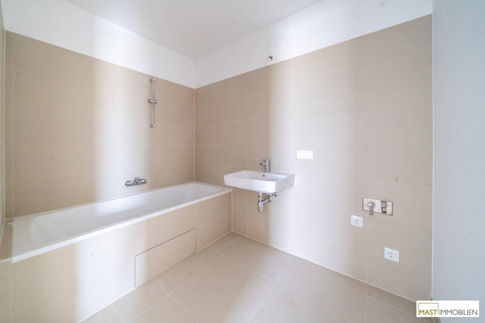 Modernes Badezimmer mit Badewanne, Waschbecken und beigefarbenen Fliesen, bereit für die Endmontage.