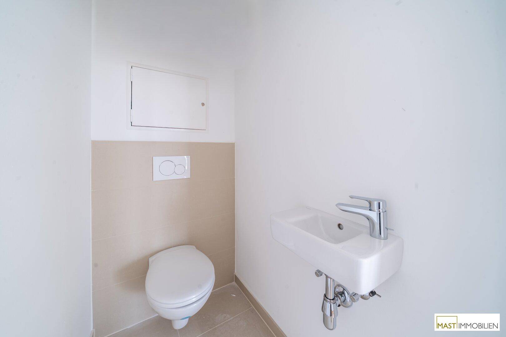 Separates Gäste-WC mit Wand-WC und kleinem Handwaschbecken, halbhoch gefliest in Beige.