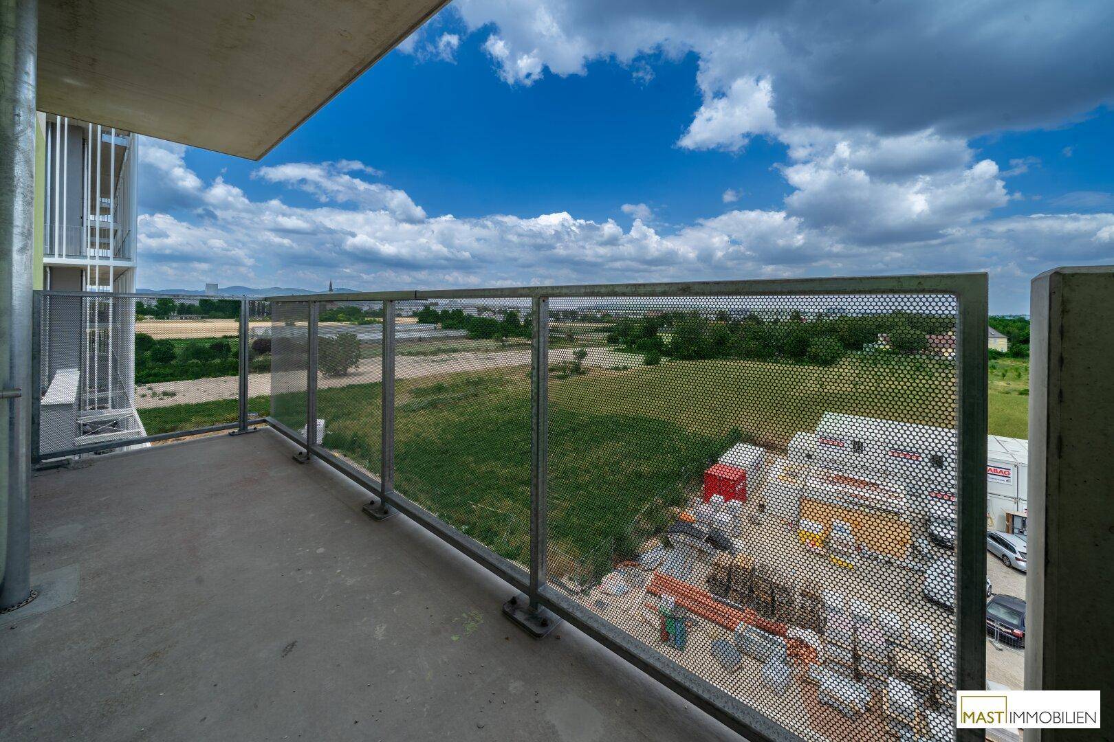 Weitläufiger Ausblick vom Balkon auf grüne Felder und die umliegende Landschaft unter blauem Himmel.