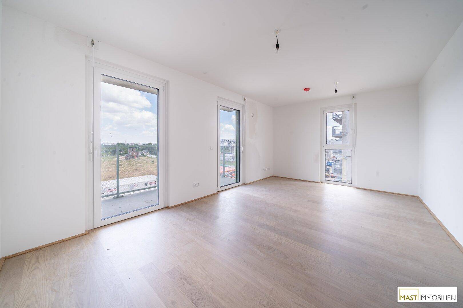 Helles, leeres Zimmer mit großen Fenstern und hellem Holzboden, bereit für die individuelle Gestaltung.