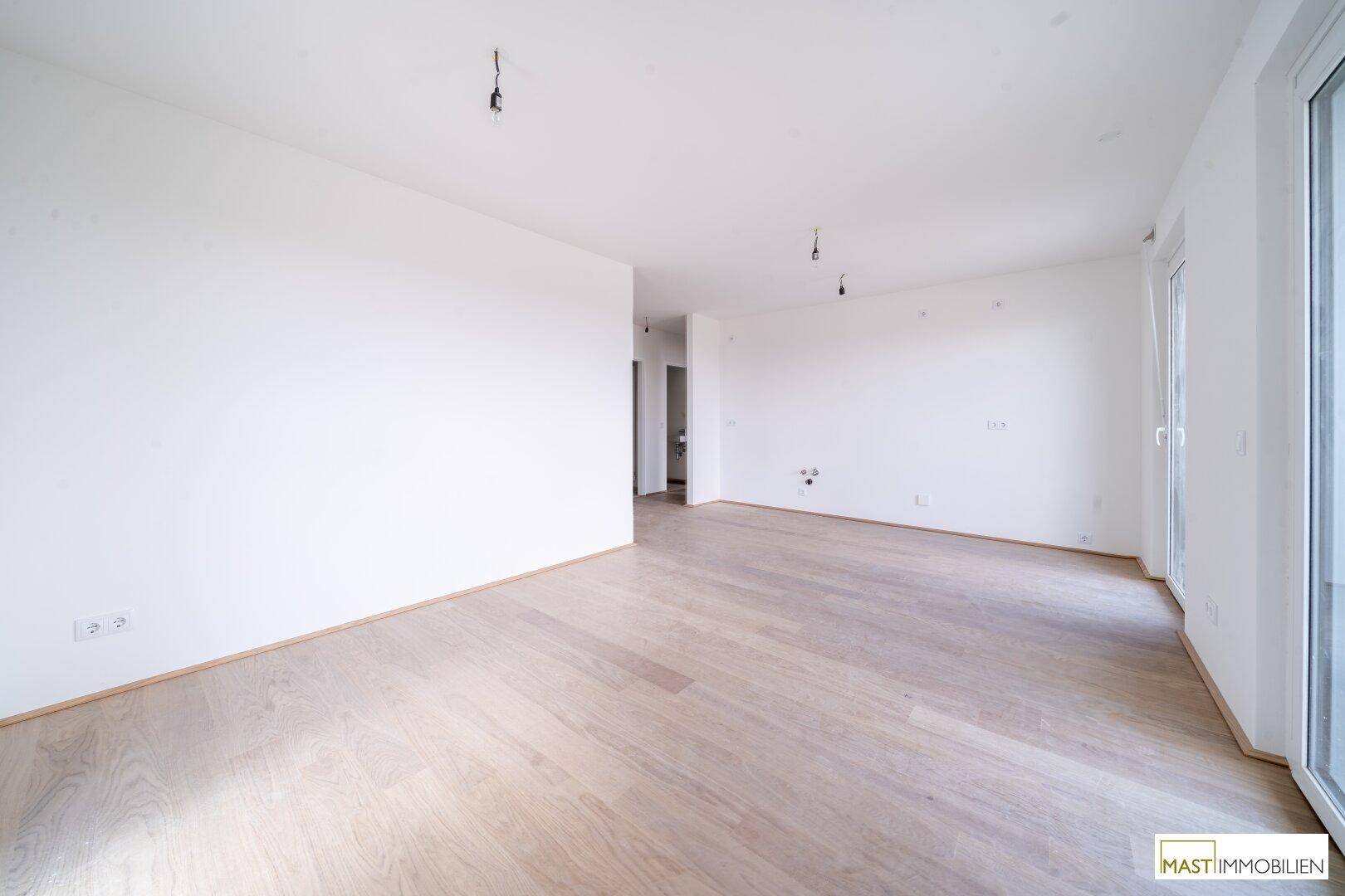 Geräumiges, unmöbliertes Zimmer mit hellem Holzboden und weißen Wänden, ideal für offene Wohnkonzepte.