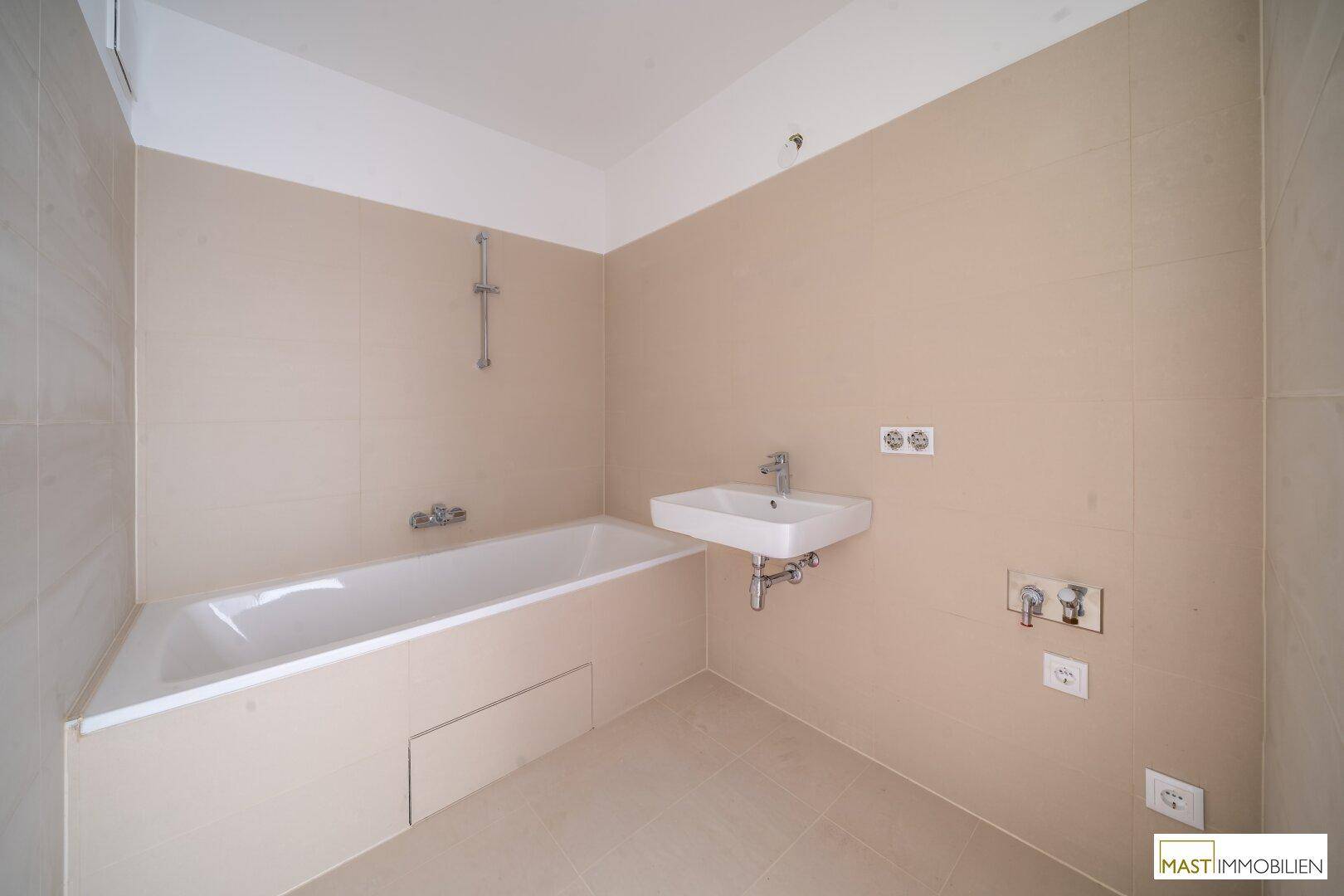 Modernes Badezimmer mit Badewanne, Waschbecken und beigefarbenen Fliesen an den Wänden.