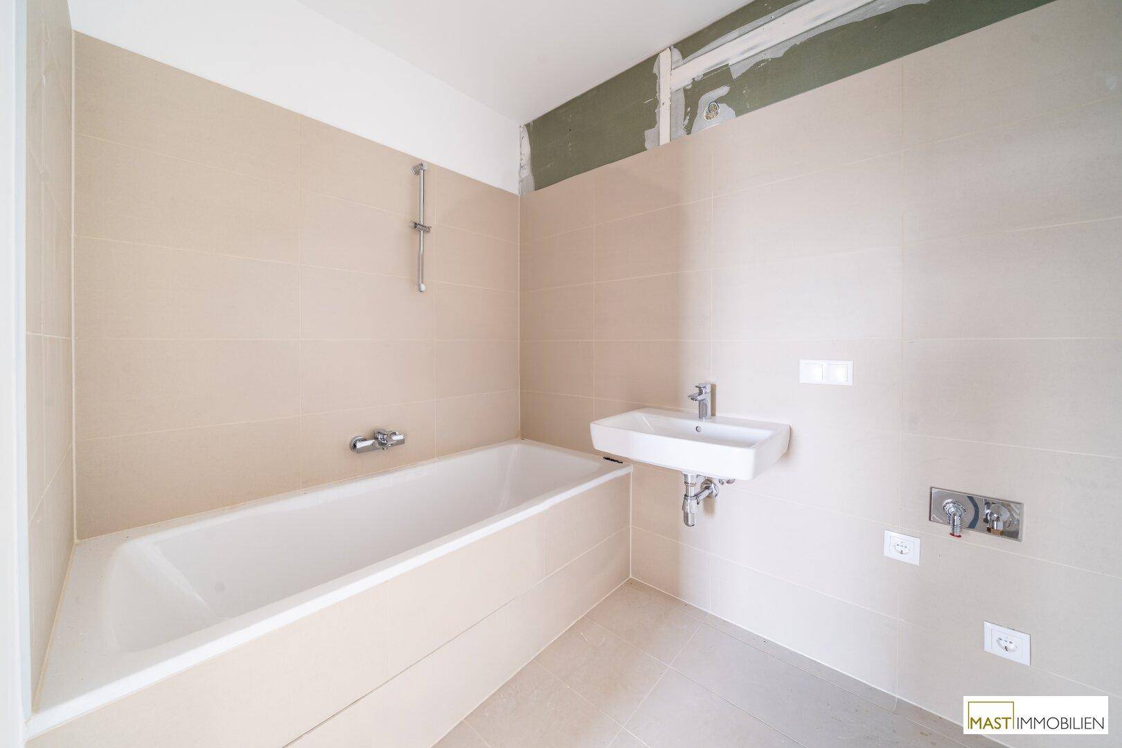 Modernes Badezimmer mit beigefarbenen Fliesen, einer Badewanne und einem einzelnen Waschbecken.