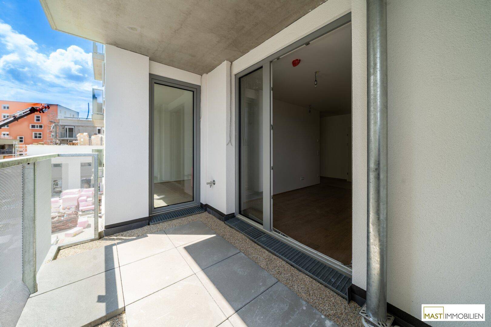Heller Balkon mit Schiebetüren zum Innenraum und Blick auf die Baustelle.