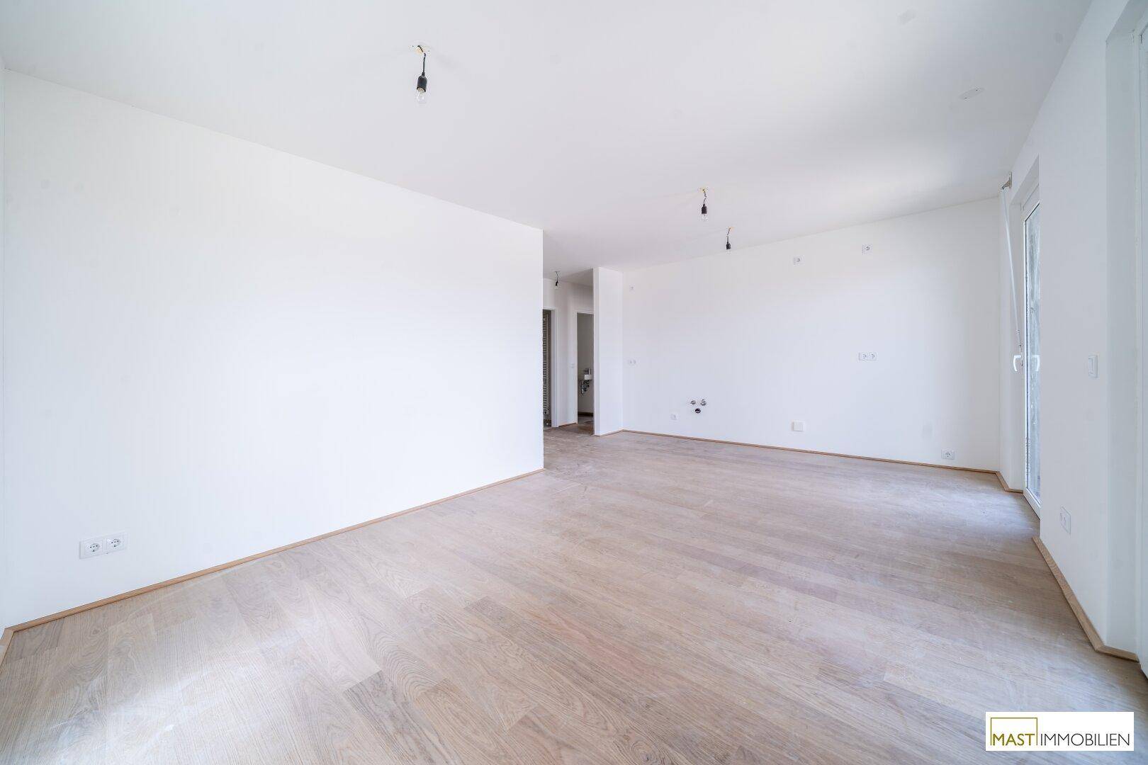 Geräumiger, heller Raum mit weiß gestrichenen Wänden und hellem Holzfußboden.