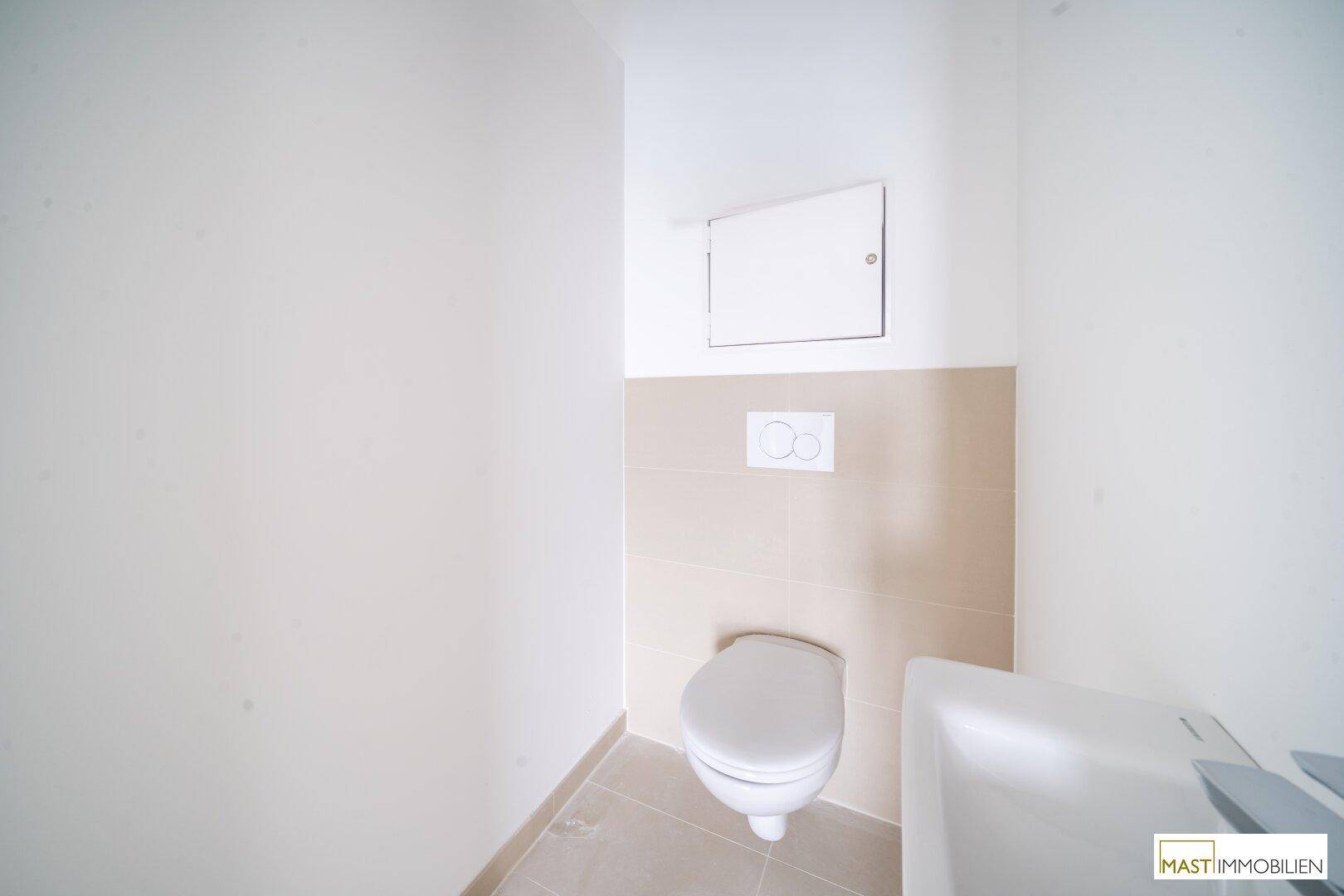 Kompaktes Gäste-WC mit wandhängender Toilette und kleinem Waschbecken, ausgestattet mit hellen Fliesen.