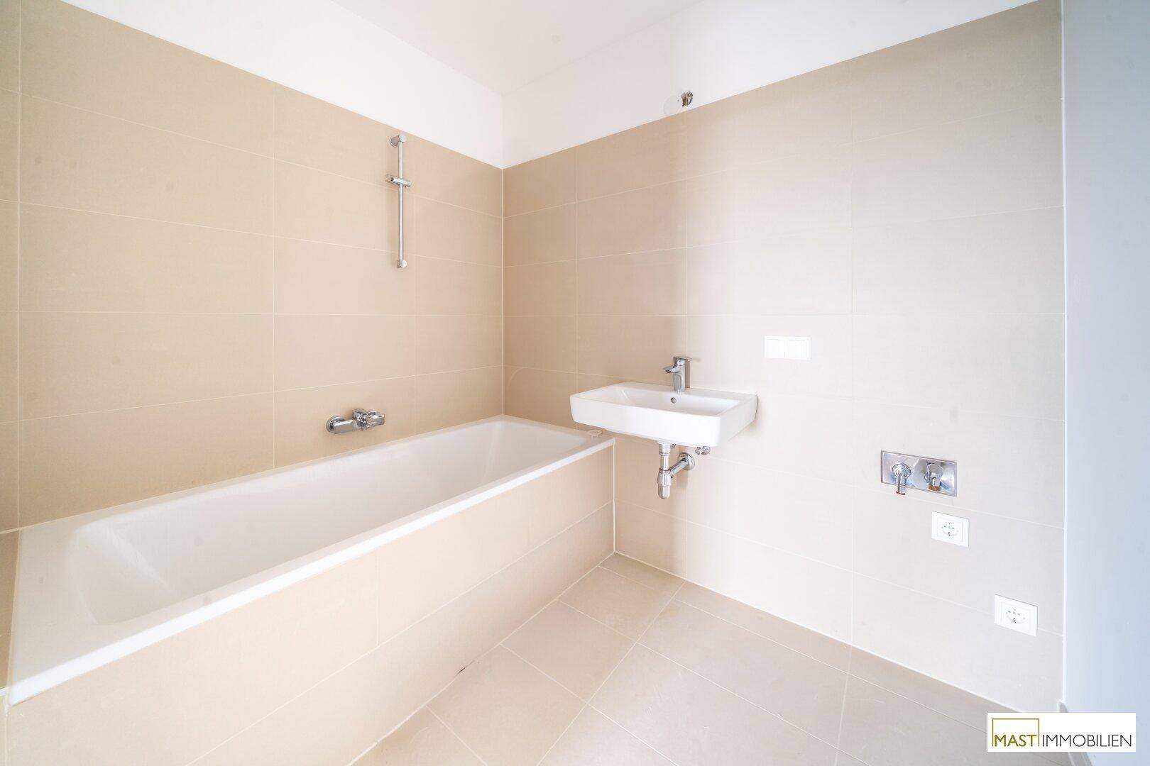 Modernes Badezimmer mit Badewanne, Einzelwaschbecken und beigefarbenen Fliesen an Wänden und Boden.