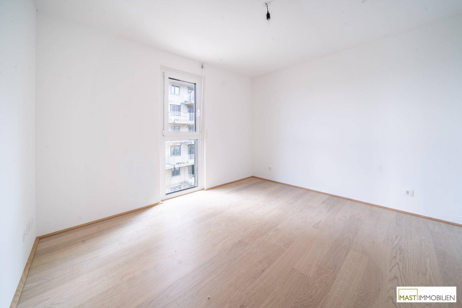 Ruhiges Schlafzimmer mit hellem Holzboden und einem großen Fenster, das den Blick auf die Umgebung freigibt.