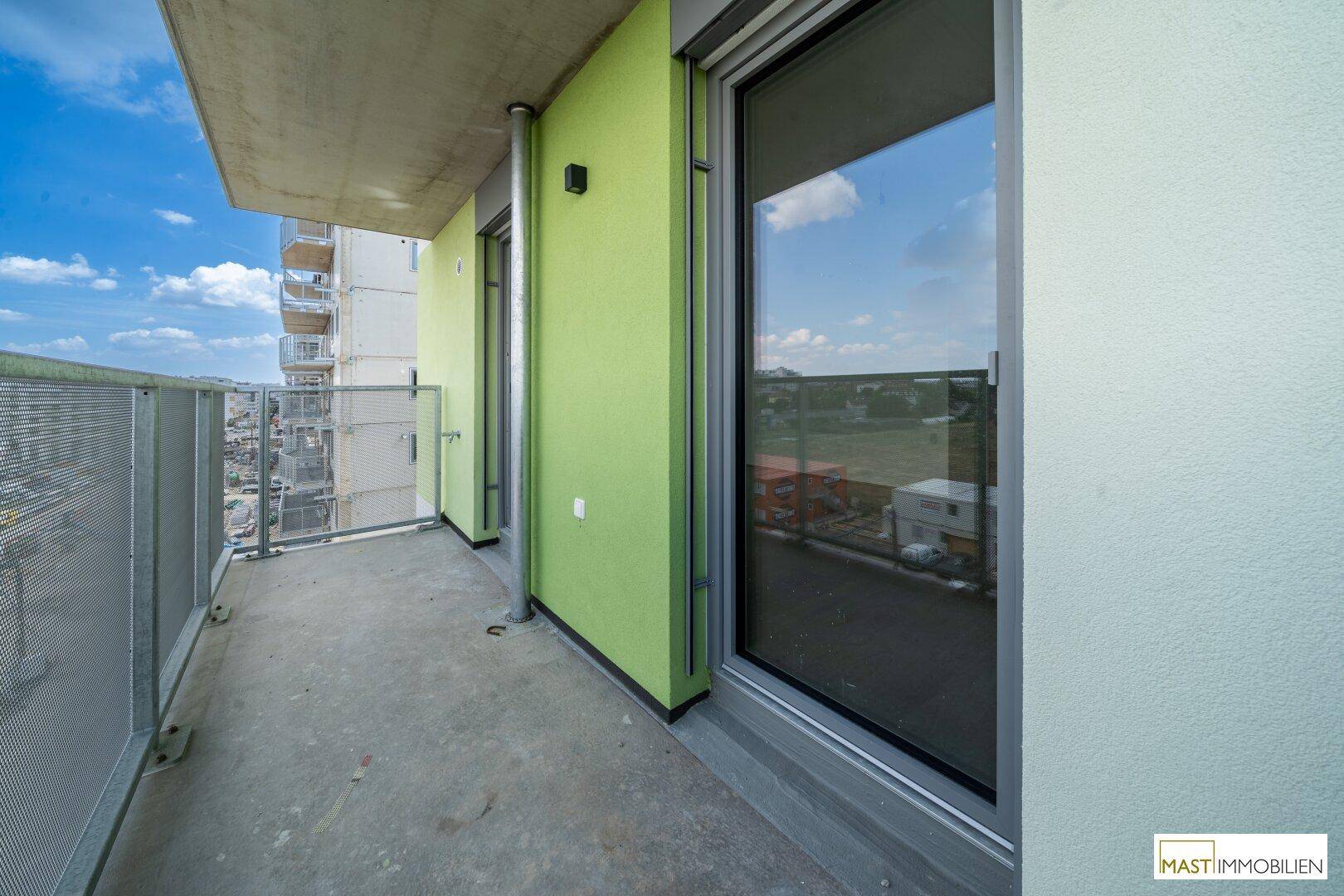 Moderner Balkon mit grüner Fassadenakzentuierung und großen Fenstern, die viel Licht in die Innenräume lassen.