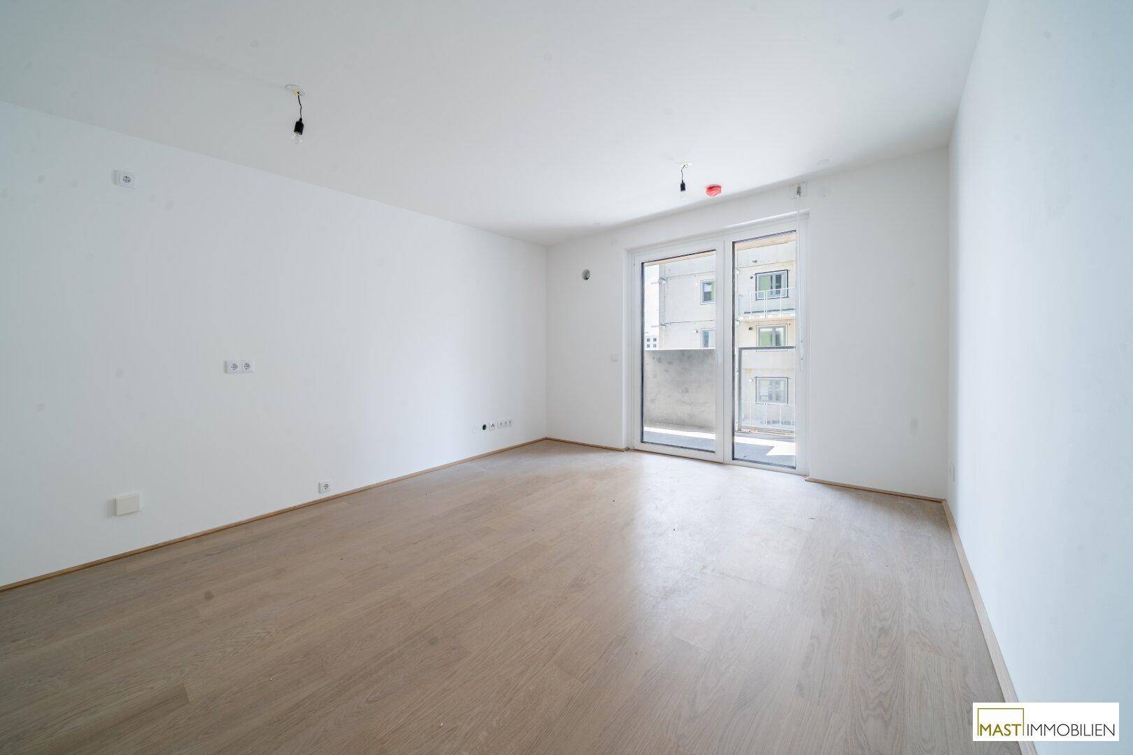 Helles, leeres Zimmer mit Parkettboden und Zugang zu einem Balkon, ideal für Wohn- oder Schlafbereich.