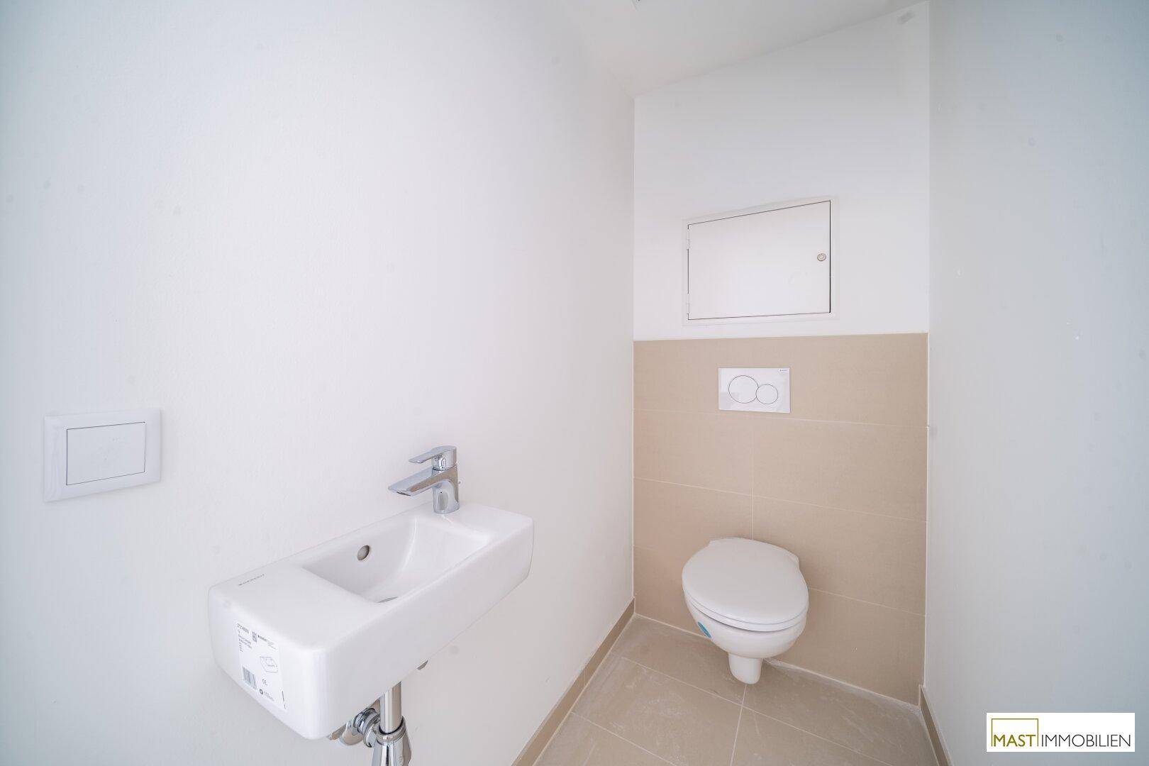 Separates Gäste-WC mit wandmontierter Toilette und kleinem Waschbecken, in neutralen Farben gehalten.