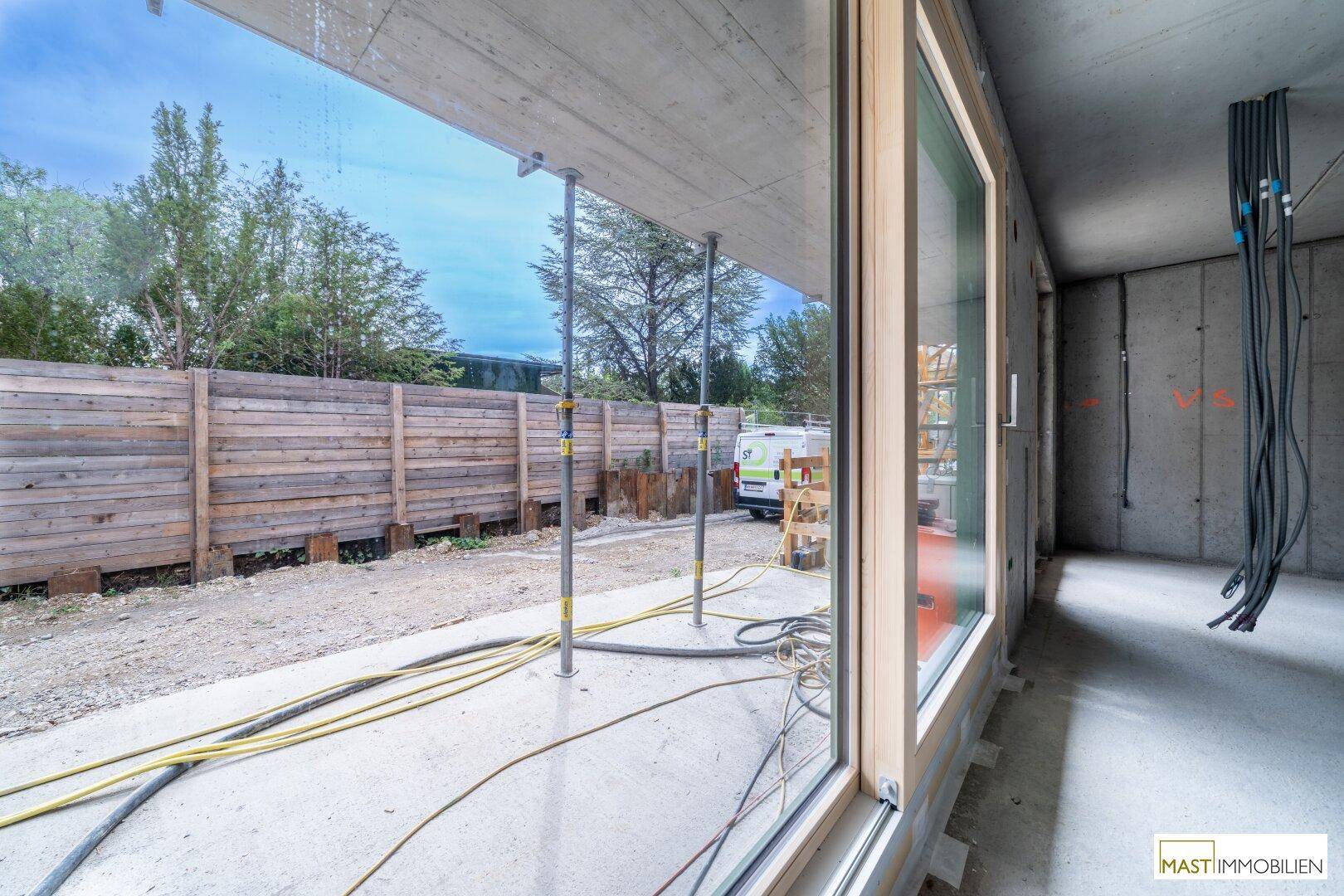 Große Fensterfront im Rohbau mit Blick auf den Außenbereich und Bauarbeiten.