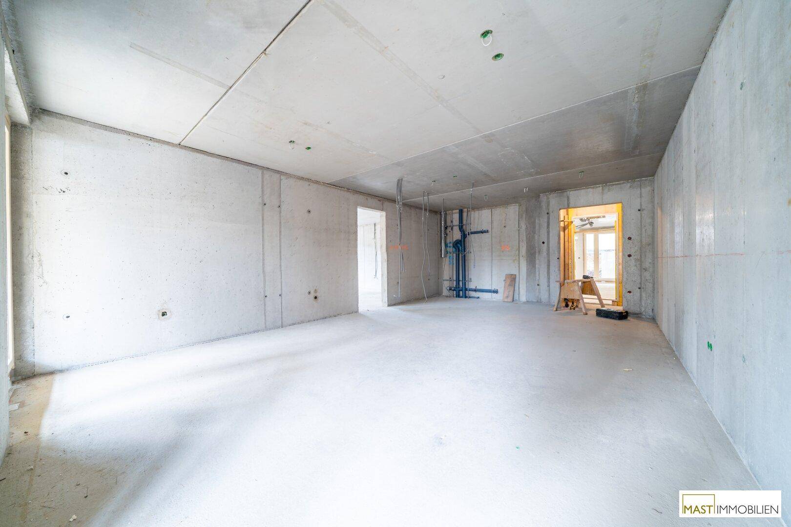Rohbau-Innenraum mit Betonwänden, sichtbaren Installationen und viel natürlichem Licht.