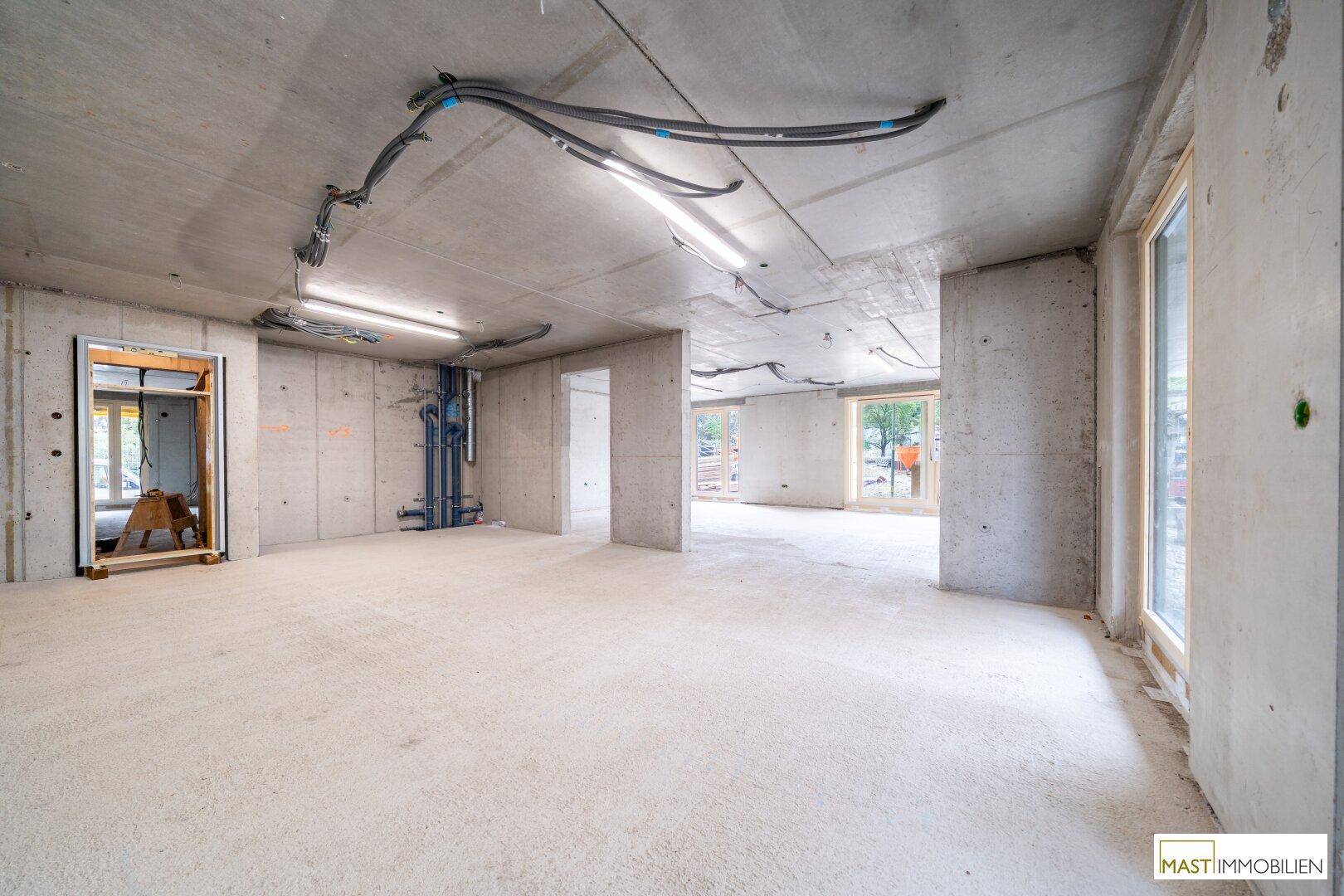 Unfertiger Innenraum im Rohbau mit Betonwänden, Decken und sichtbaren Installationen.