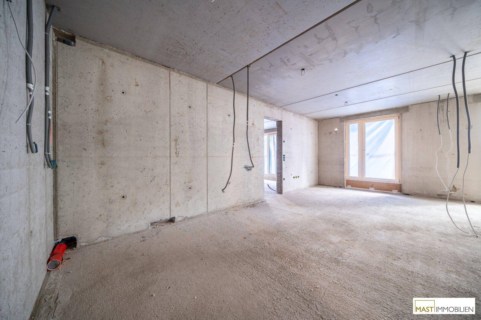 Innenansicht eines Rohbaus mit sichtbaren Leitungen und Fenstern, die auf den finalen Ausbau warten.