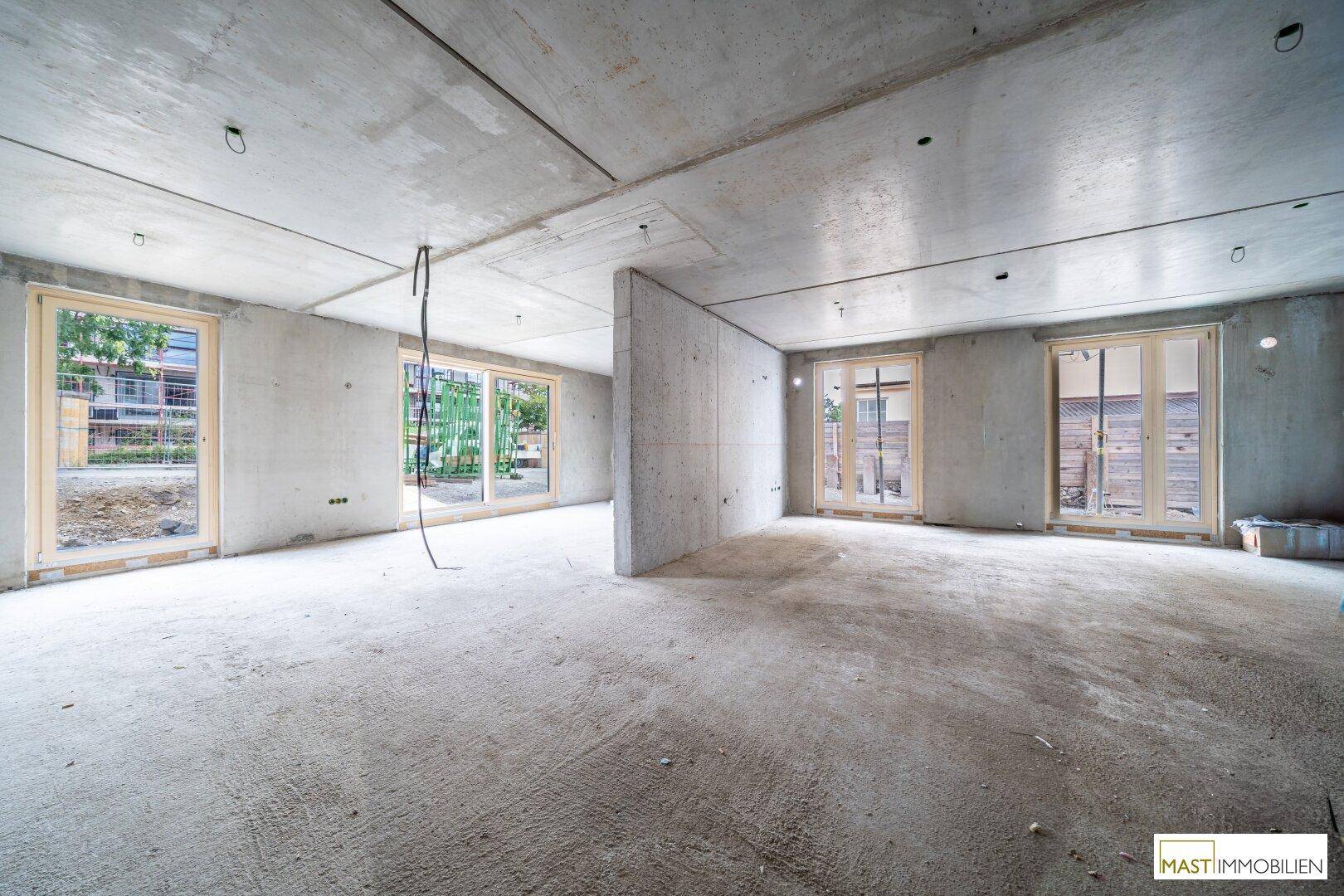 Unfertiger Innenraum mit Betonwänden und großen Fensteröffnungen, bereit für den Ausbau.