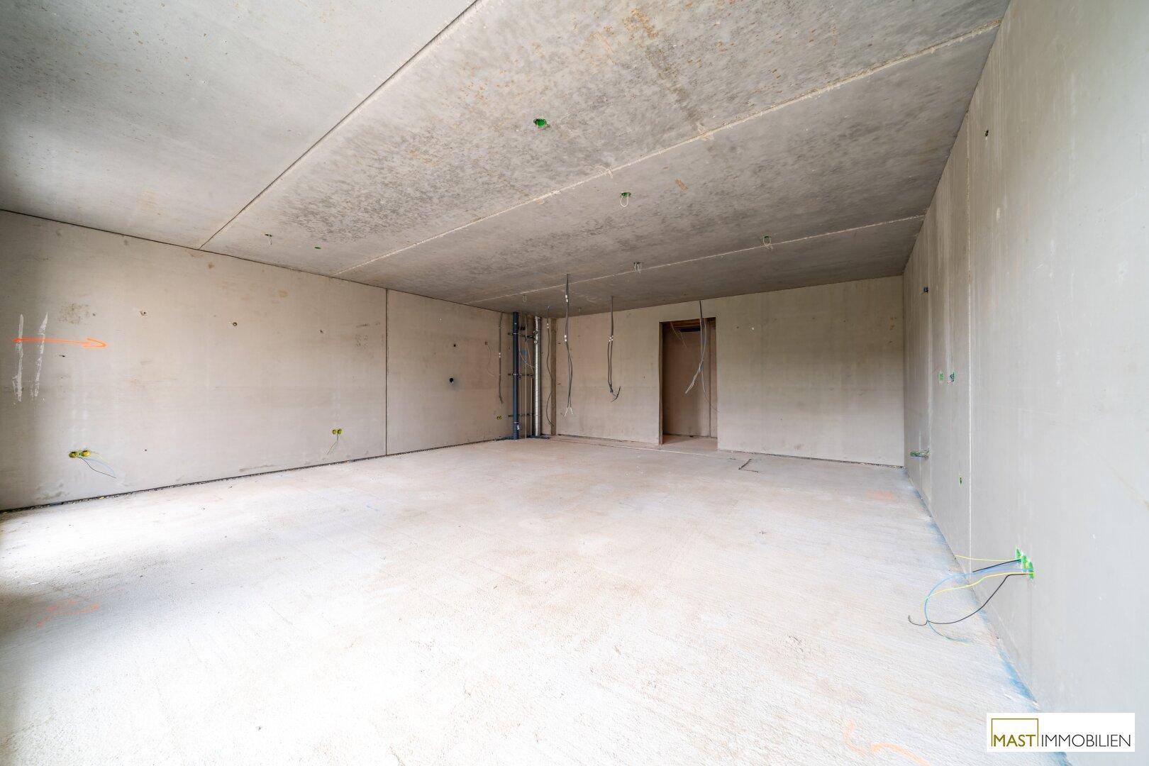 Geräumiger Rohbau-Innenraum mit Betonwänden und -decke, bereit für den weiteren Ausbau und die Gestaltung.