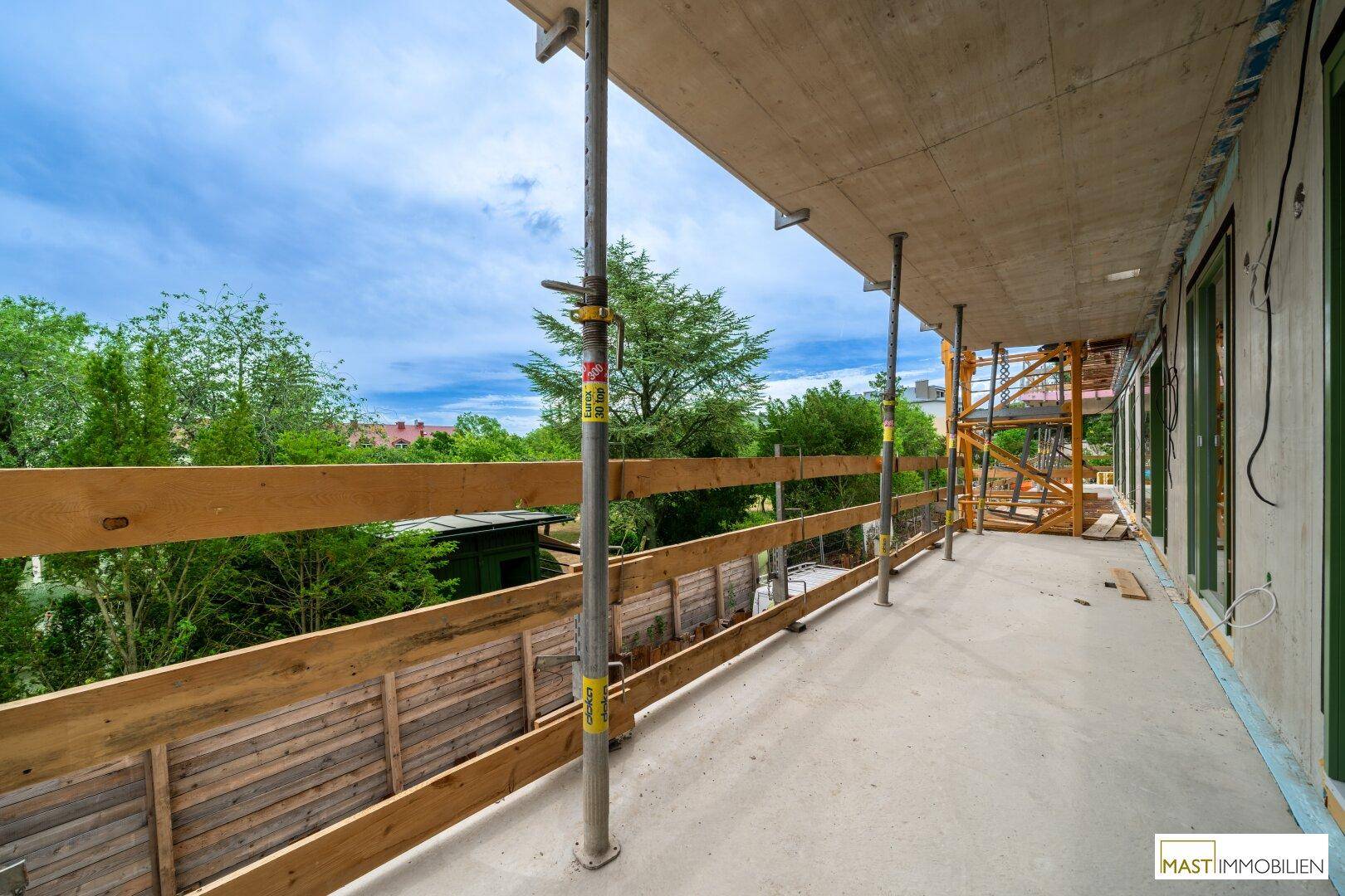 Langer Balkon im Rohbau mit provisorischem Geländer und weitem Blick auf die grüne Umgebung.