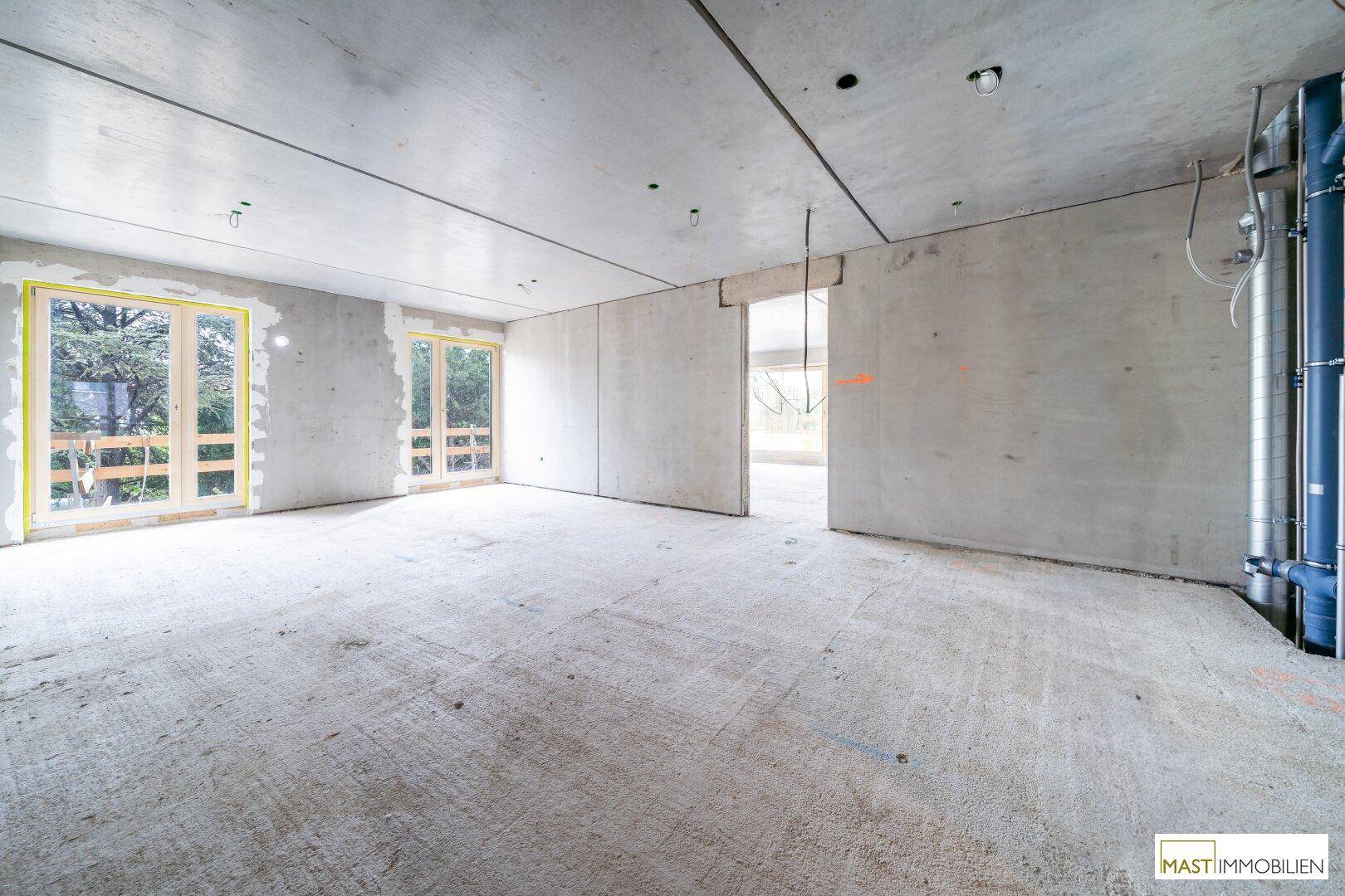 Rohbau-Innenraum mit Betonwänden, sichtbaren Installationen und Fenstern zur Außenseite.