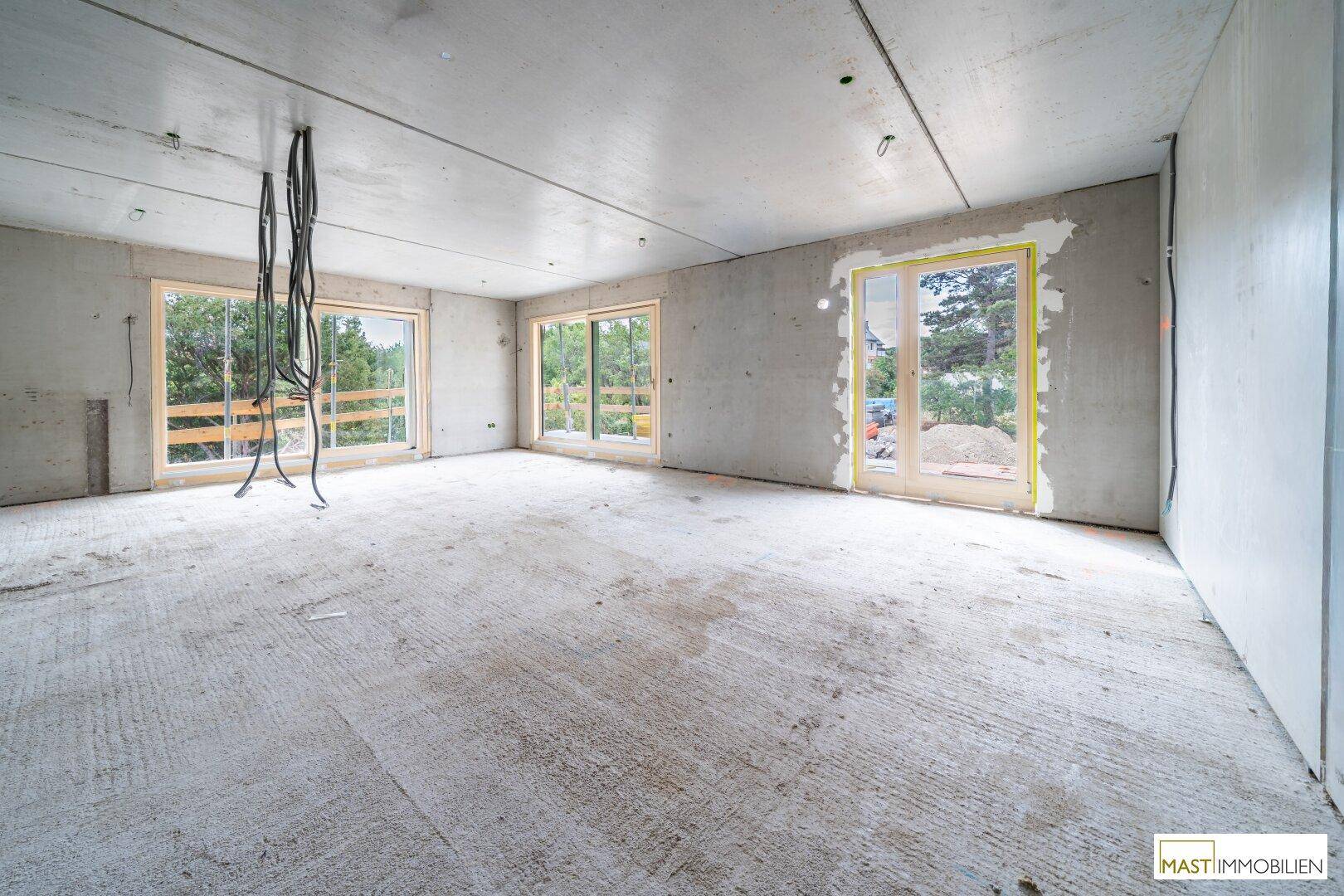 Geräumiger Rohbau-Raum mit großen Fenstern und hängenden Kabeln, bereit für den Innenausbau.