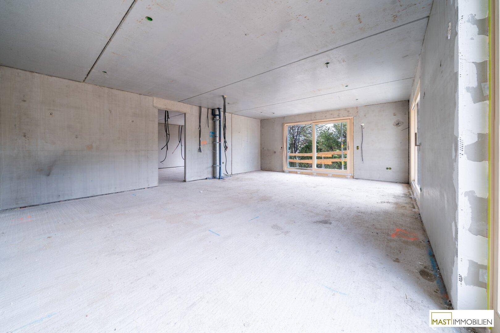 Innenraum im Rohbauzustand mit Betonoberflächen und Fenstern, die Tageslicht hereinlassen.