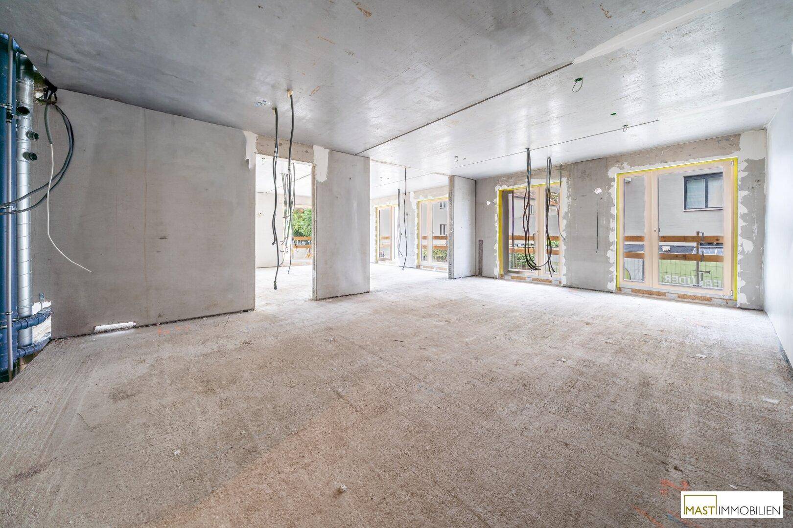 Großer, unfertiger Innenraum eines Neubaus mit Betonwänden und sichtbaren Installationen.