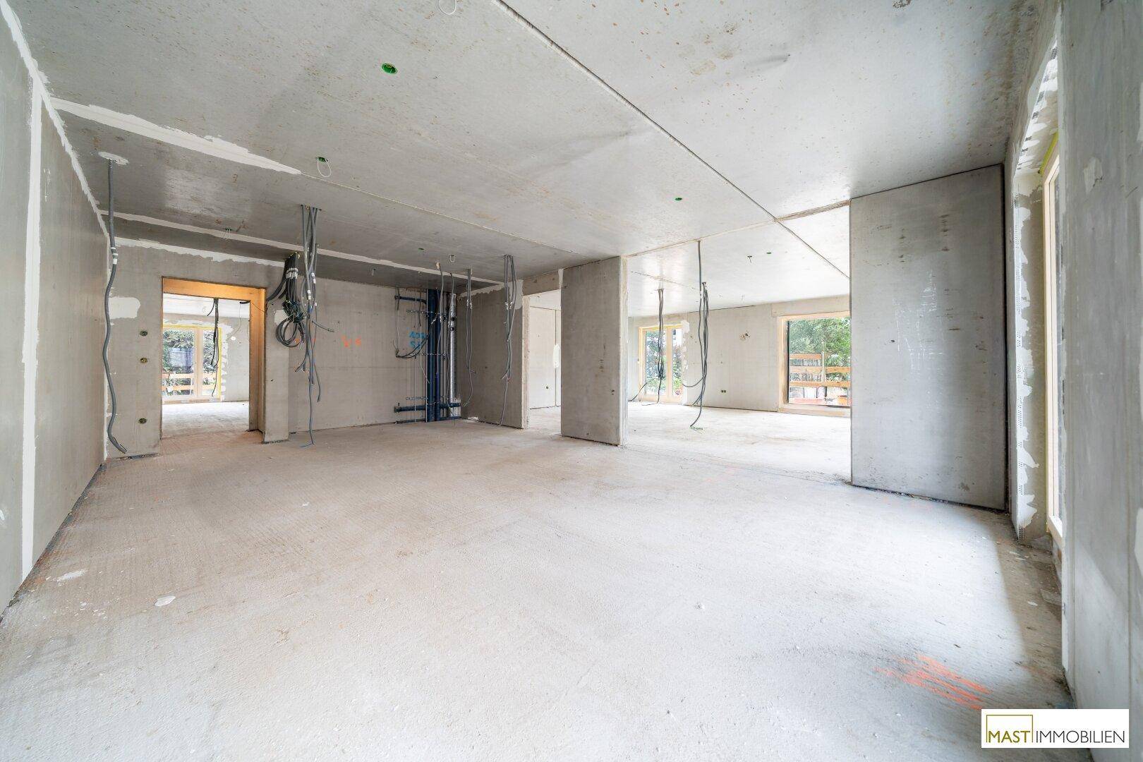 Heller Rohbau-Innenraum mit Betonwänden, sichtbaren Leitungen und viel Tageslicht.